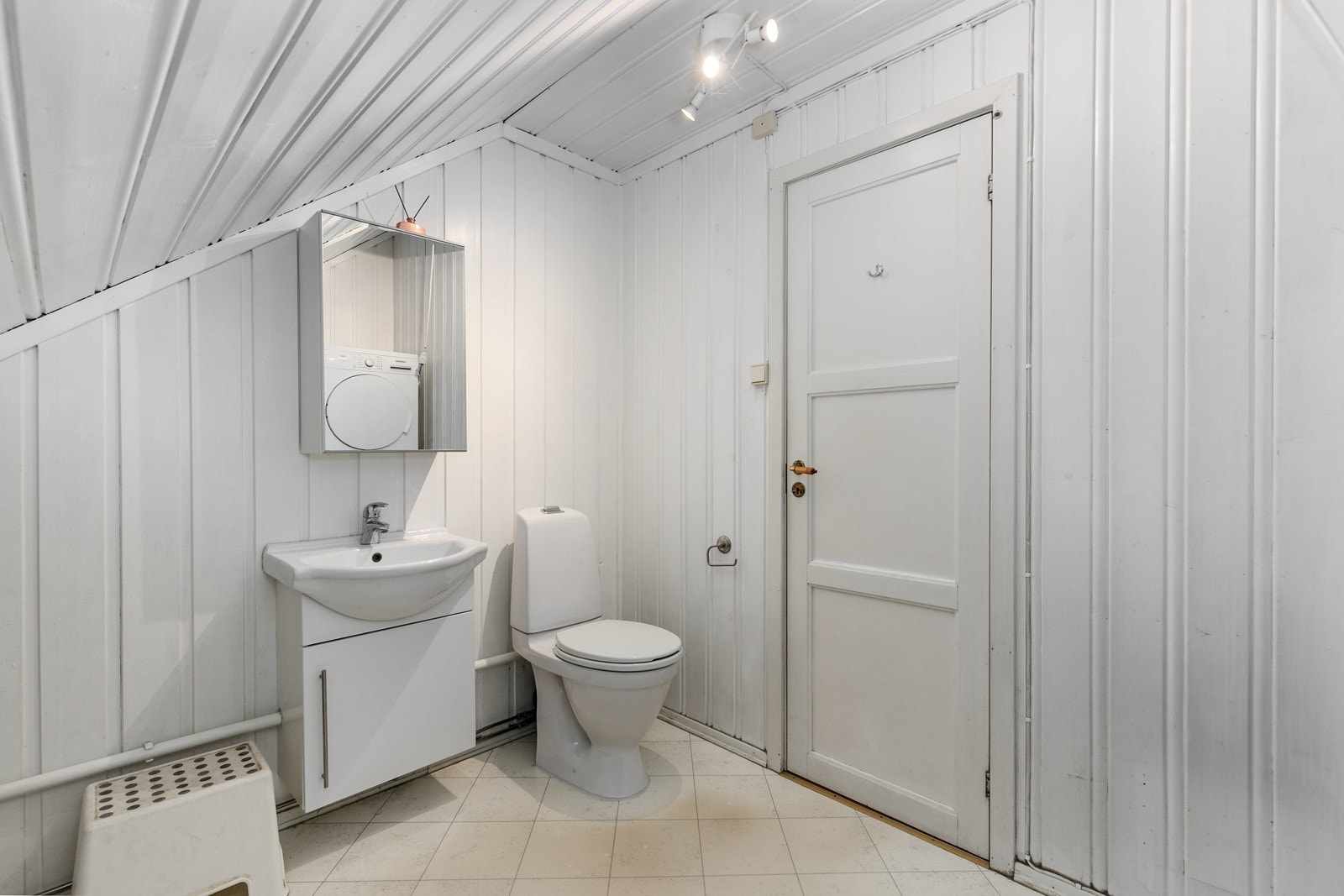 Praktisk toalettrom i boligens 2. etasje med hvitmalt panel på vegg- og i himling, samt belegg på gulv. Innredningen består av servantmøblement, speilskap og toalett. Galleribilde