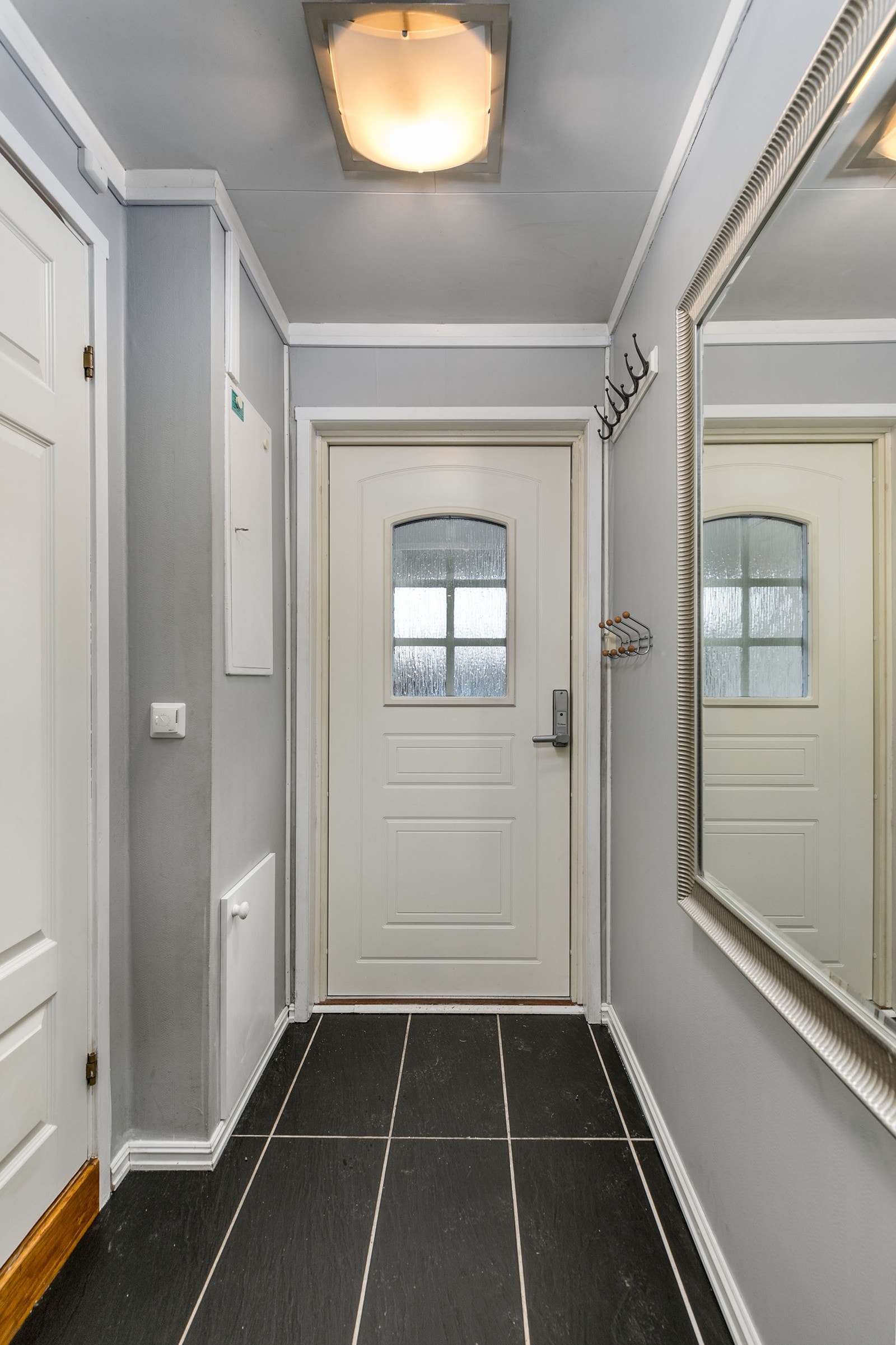 En tiltalende entre med fliser på gulv med gulvvarme og lysmalte veggflater ønsker deg velkommen inn. Galleribilde