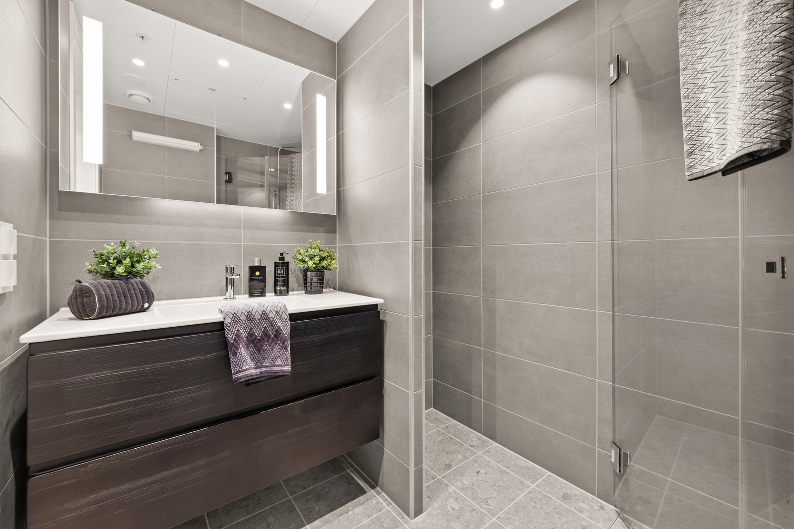 Det er innredet med skuffeseksjon m/heldekkende servant, speil med integrert belysning, vegghengt toalett og dusjdører Galleribilde