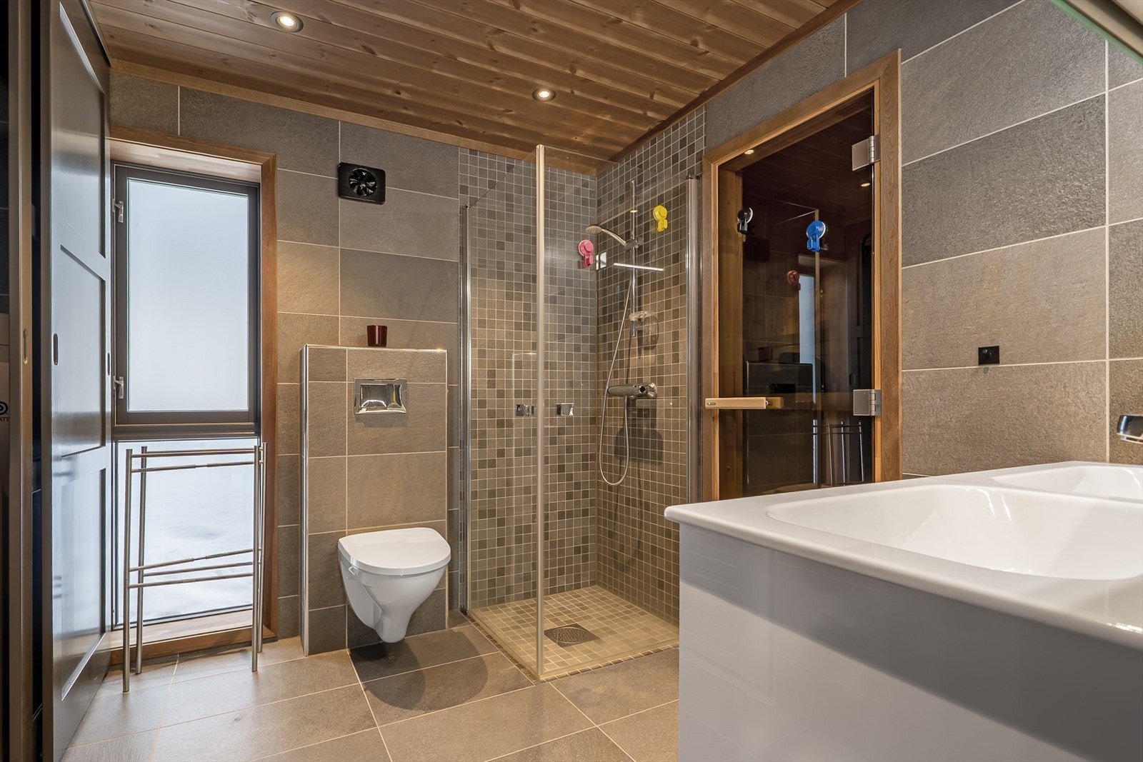 På badet er det dusj med flis på vegg og tilhørende badstue. Bak skyvedører har bla vaskemaskin. Galleribilde