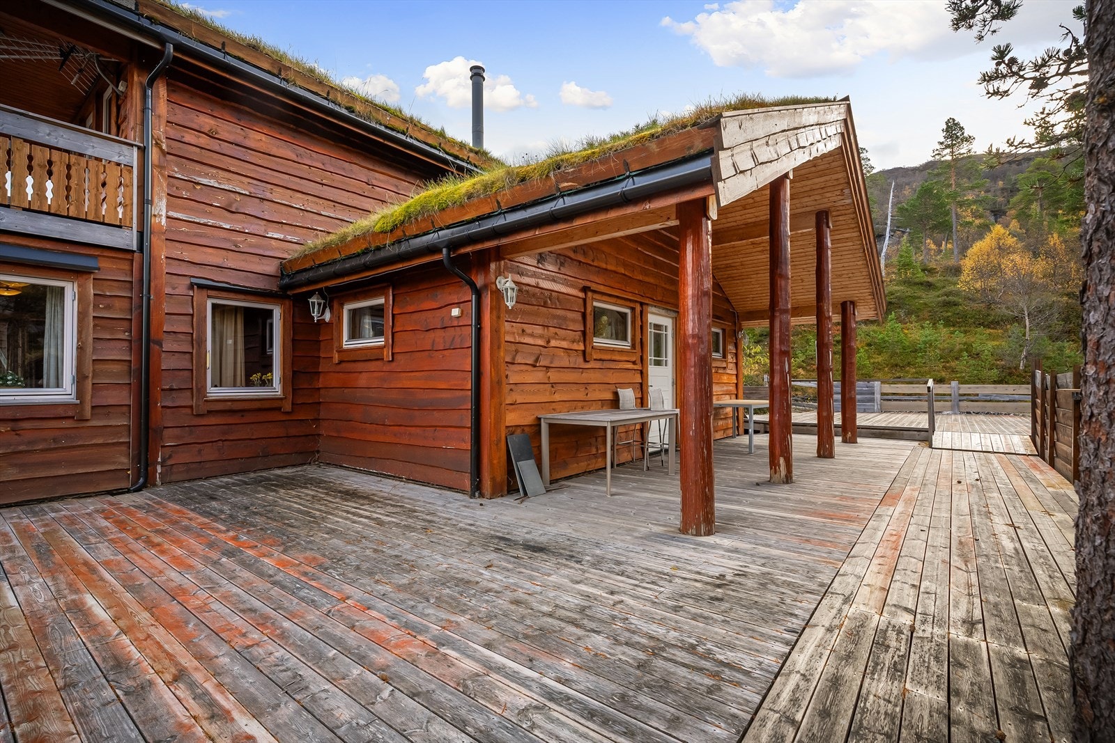 Stor terrasse som går rundt to av sidene til hytten Galleribilde