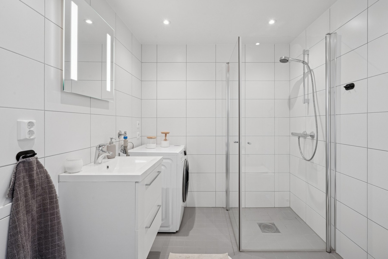 Lyst og moderne bad med opplegg for vaskemaskin og tørketrommel. Dusjen har innfellbare glassdører som bidrar til å gi en mer romslig følelse. Galleribilde