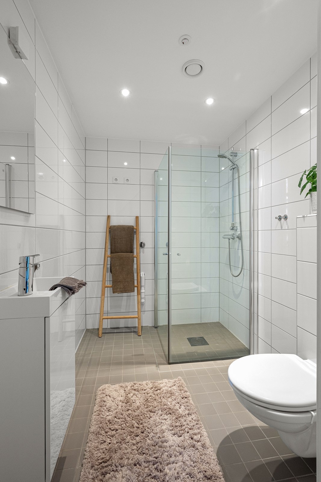 Lekkert og flislagt bad med gulvvarme. Plass og opplegg for vaskemaskin og tørketrommel. Badet består av servant med underskap, veggmontert toalett, dusjhjørne med nedfelt dusjssone, og speil på vegg med mulighet for installering av lys Galleribilde