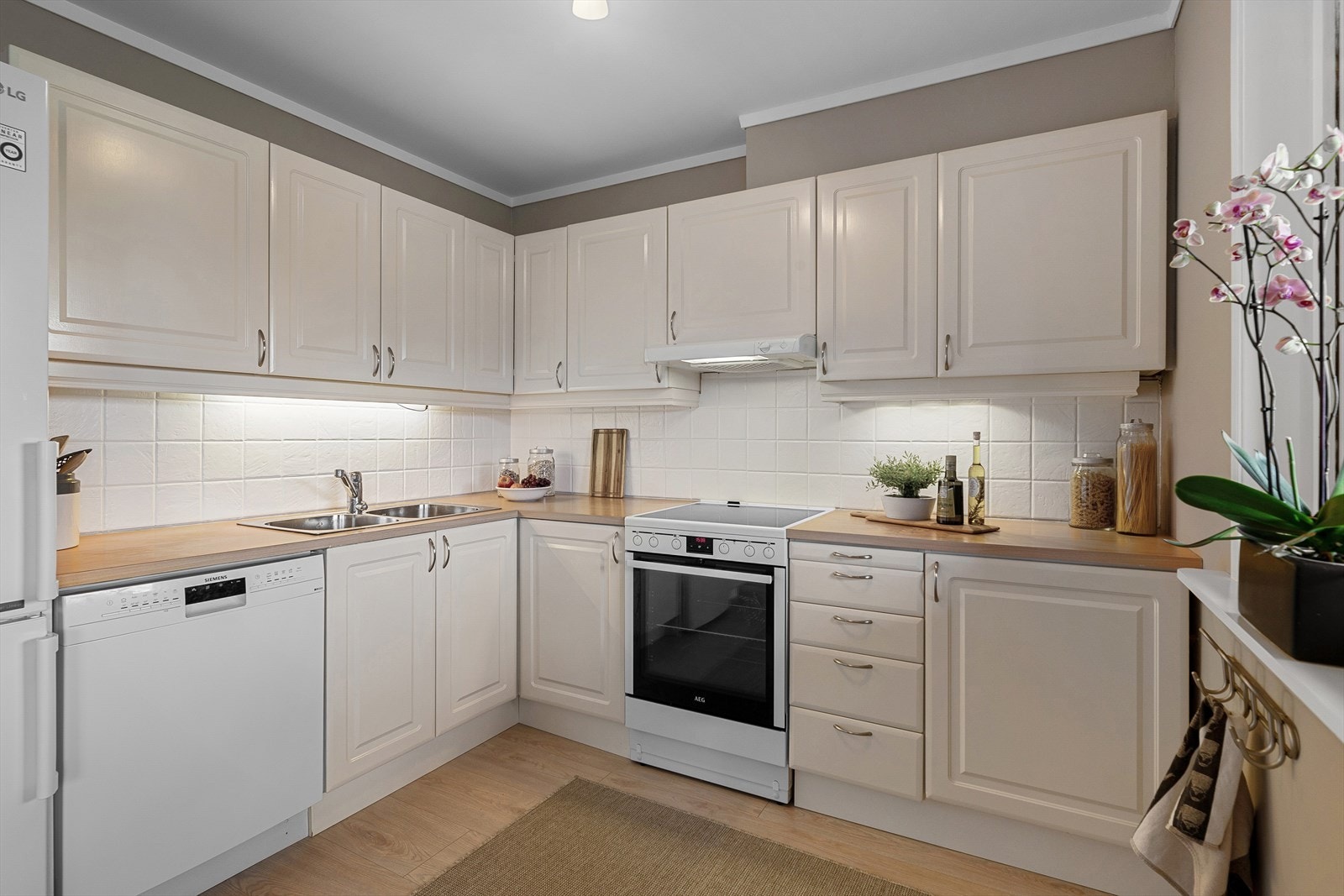 Delikat kjøkkeninnredning med lyse profilerte fronter, benkeplate av laminat og flissatt vegg over benkeplaten. Galleribilde