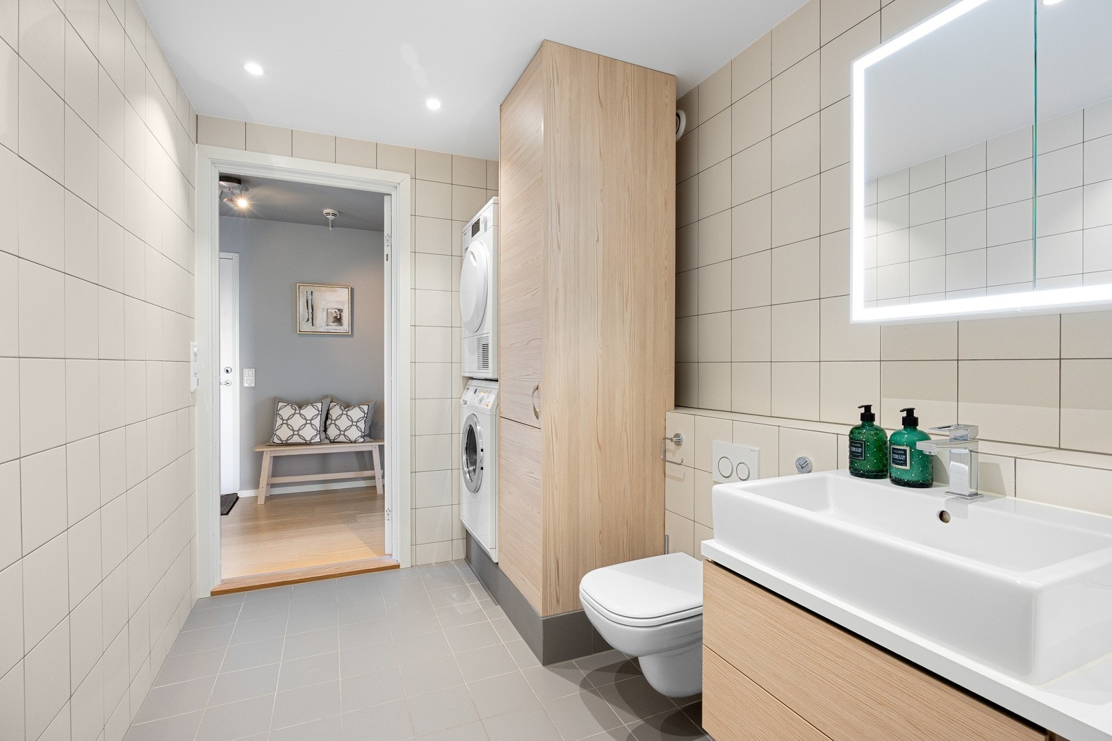 Servantseksjon med skuffer og porselenvask.Speilskap med lys, vegghengt wc, høyskap, elektrisk hånkletørker, samt opplegg for vaskemaskin og tørketrommel. Galleribilde