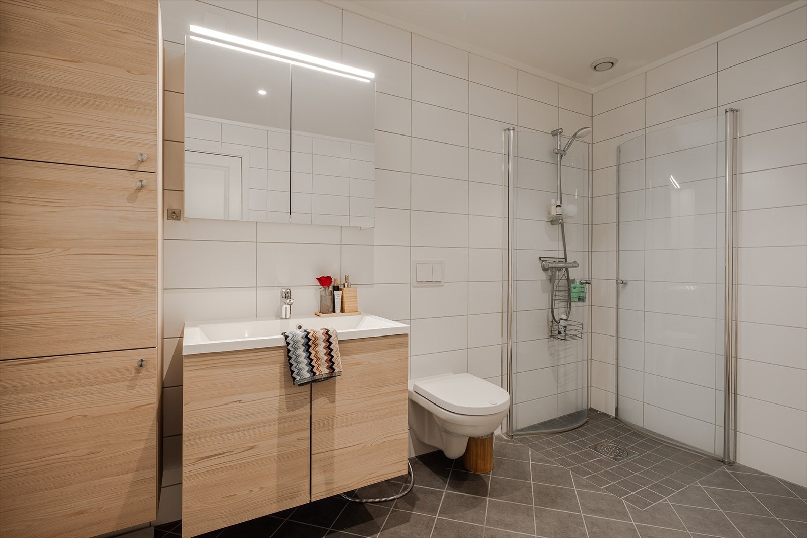 Badet har veggmontert toalett, dusjhjørne med glassvegger og veggmontert dusj, samt opplegg for vaskemaskin. Galleribilde