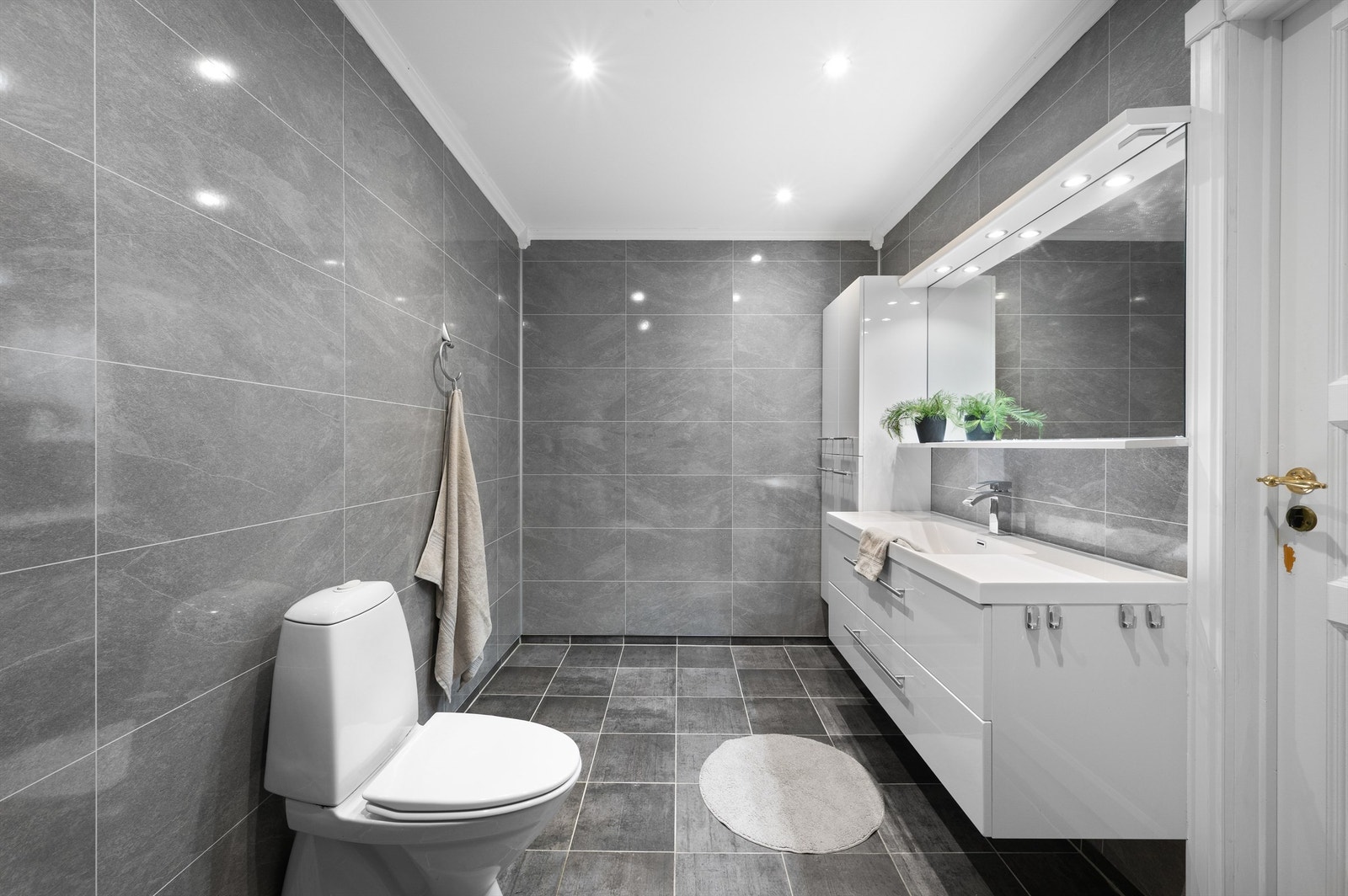 Stort bad med fliser og varmekabler på gulv, baderomsplater på vegg, spotter i tak og klassisk badromsinnredning med gode oppbevaringsmuligheter. Galleribilde