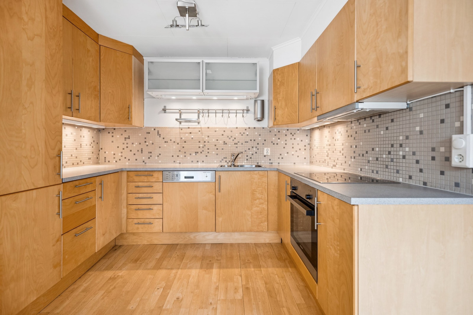 Glatte fronter på skapene og laminert benkeplate. Det er flislagt mellom benk og overskap samt godt med belysning under overskap Galleribilde