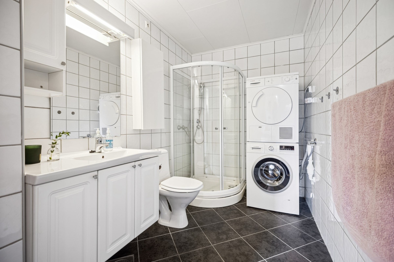 Pent flislagt bad med gulvvarme, heldekkende servant, skap og speil med belysning, dusjkabinett med glassdører og opplegg for vaskemaskin/tørketrommel Galleribilde