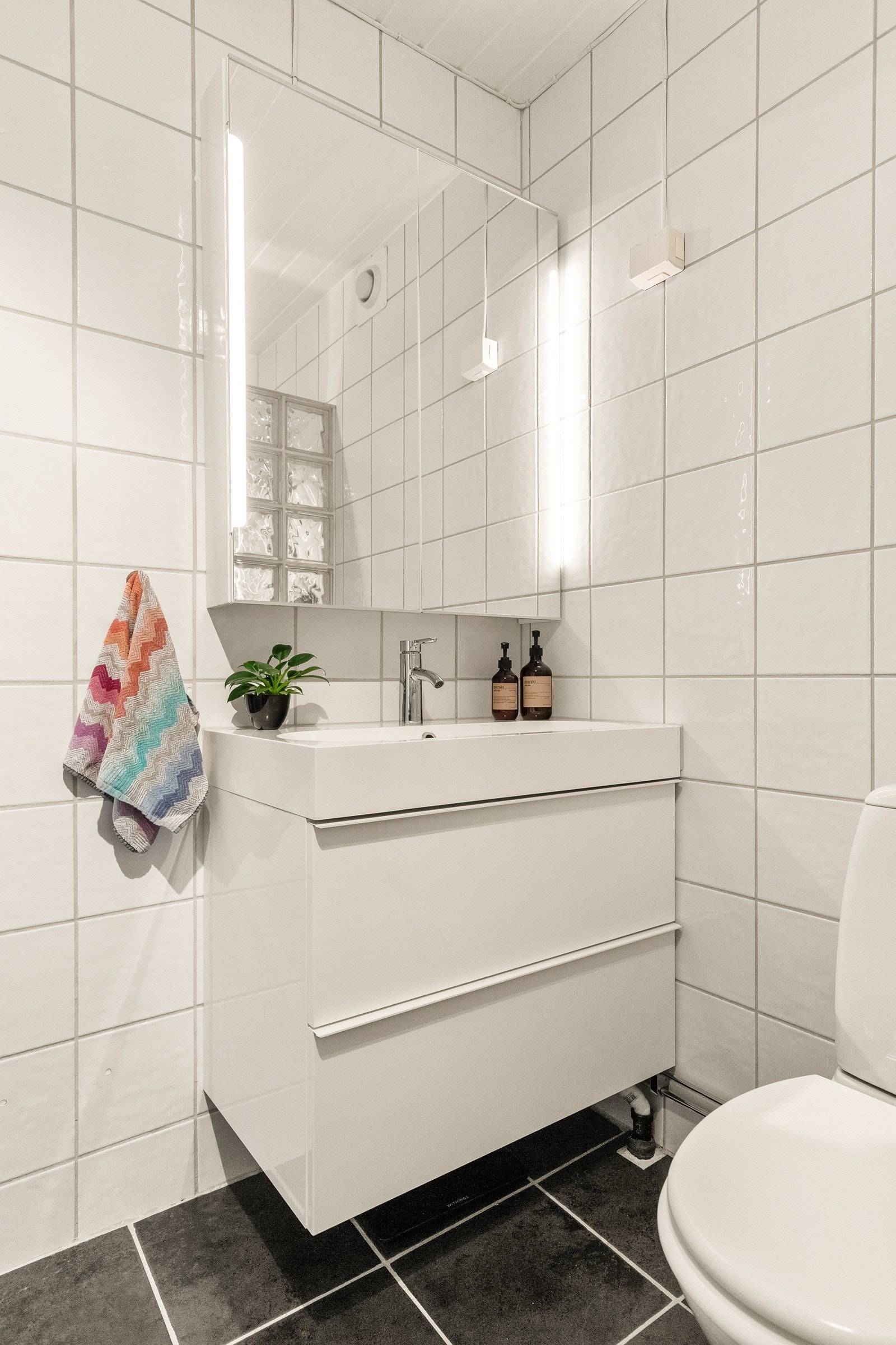 Baderommet er tidløst og holder et stilrent design med lyse fliser på vegg og mørke på gulv. Galleribilde