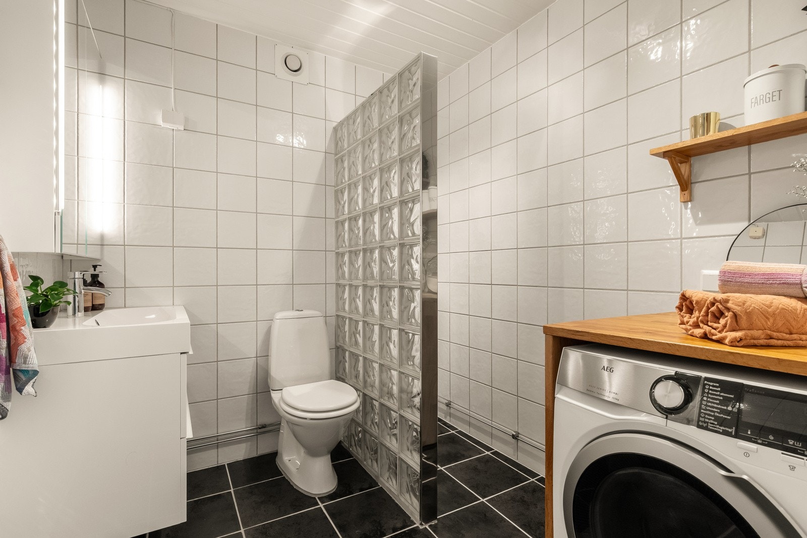 Lyst og pent baderom som inneholder dusjhjørne, benkeskap med heldekkende servant, speilskap og opplegg for vaskemaskin. Galleribilde