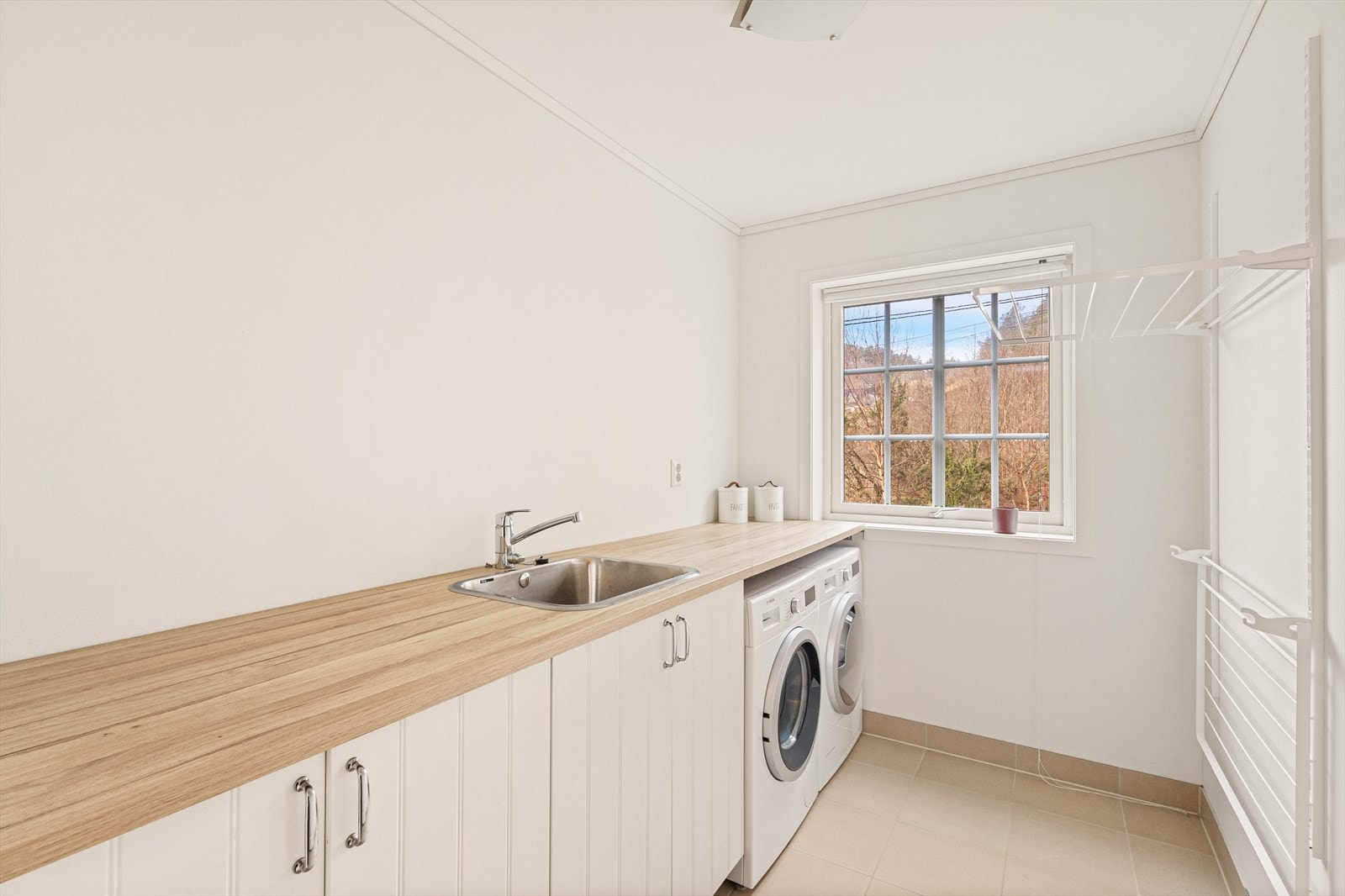 Vaskerommet er praktisk innredet med opplegg for vaskemaskin og tørketrommel, tørkestativ samt en laminert benkeplate med vask og oppbevaringsløsninger Galleribilde