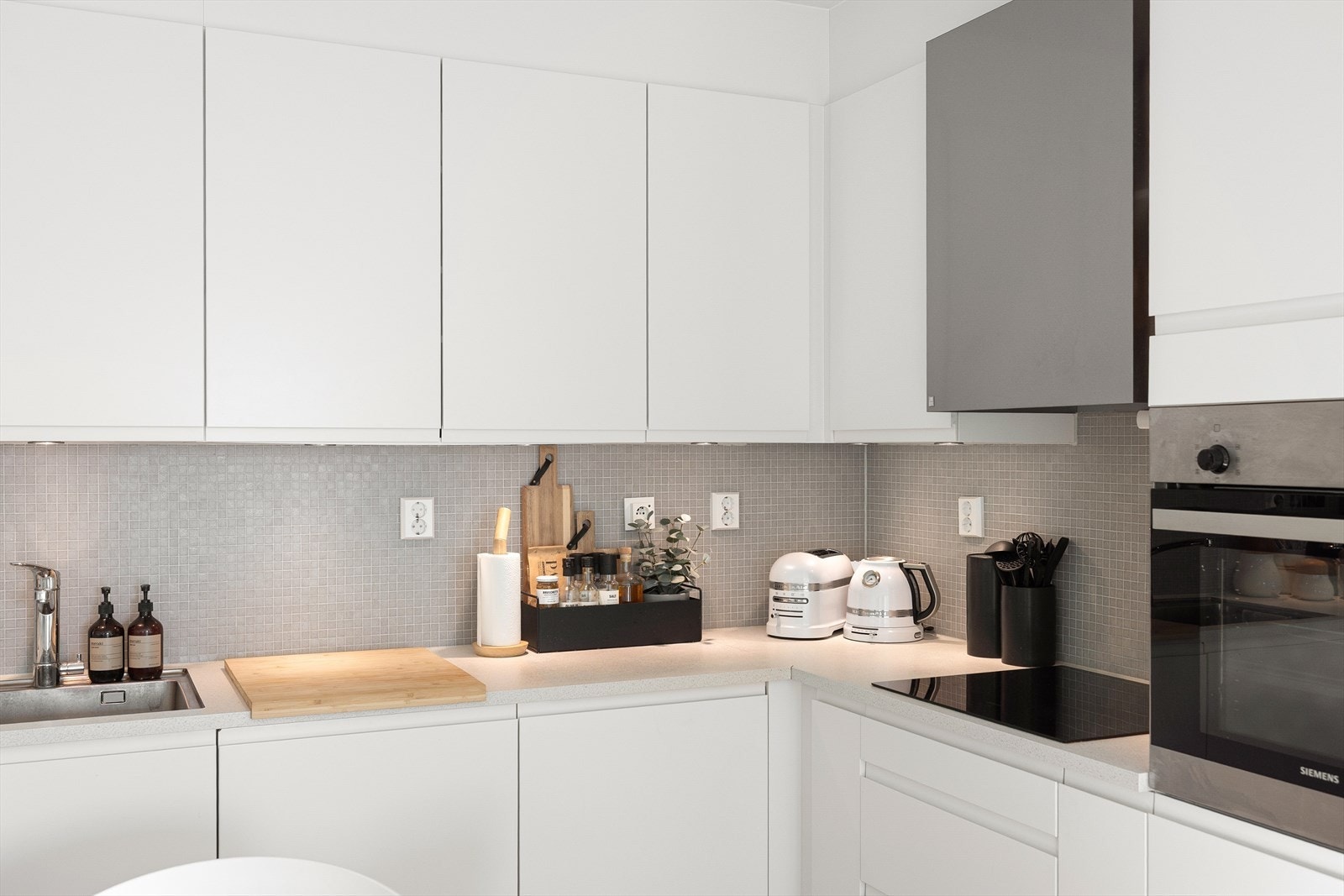 Mellom benken og overskapene er det grå glassmosaikkfliser, benkeplaten er av laminat, og vasken er i rustfritt stål Galleribilde