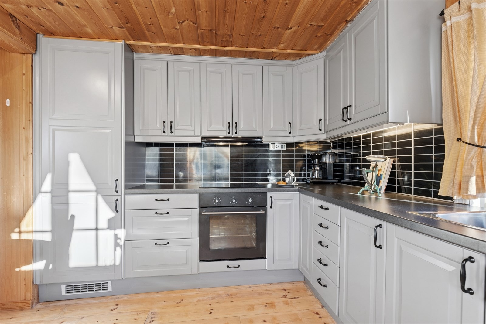 Kjøkkeninnredning med lys gråmalte, profilerte fronter. Laminat benkeplate og backsplash mellom benkeplaten og overskap. Galleribilde