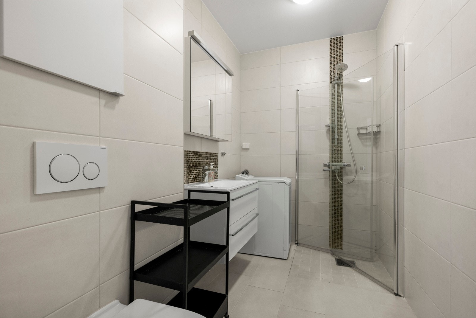 Flislagt baderom med gulvvarme fra 2018. Store, lyse fliser skaper et stilrent uttrykk, supplert med detaljfliser i dusjsonen og bak servanten. Galleribilde