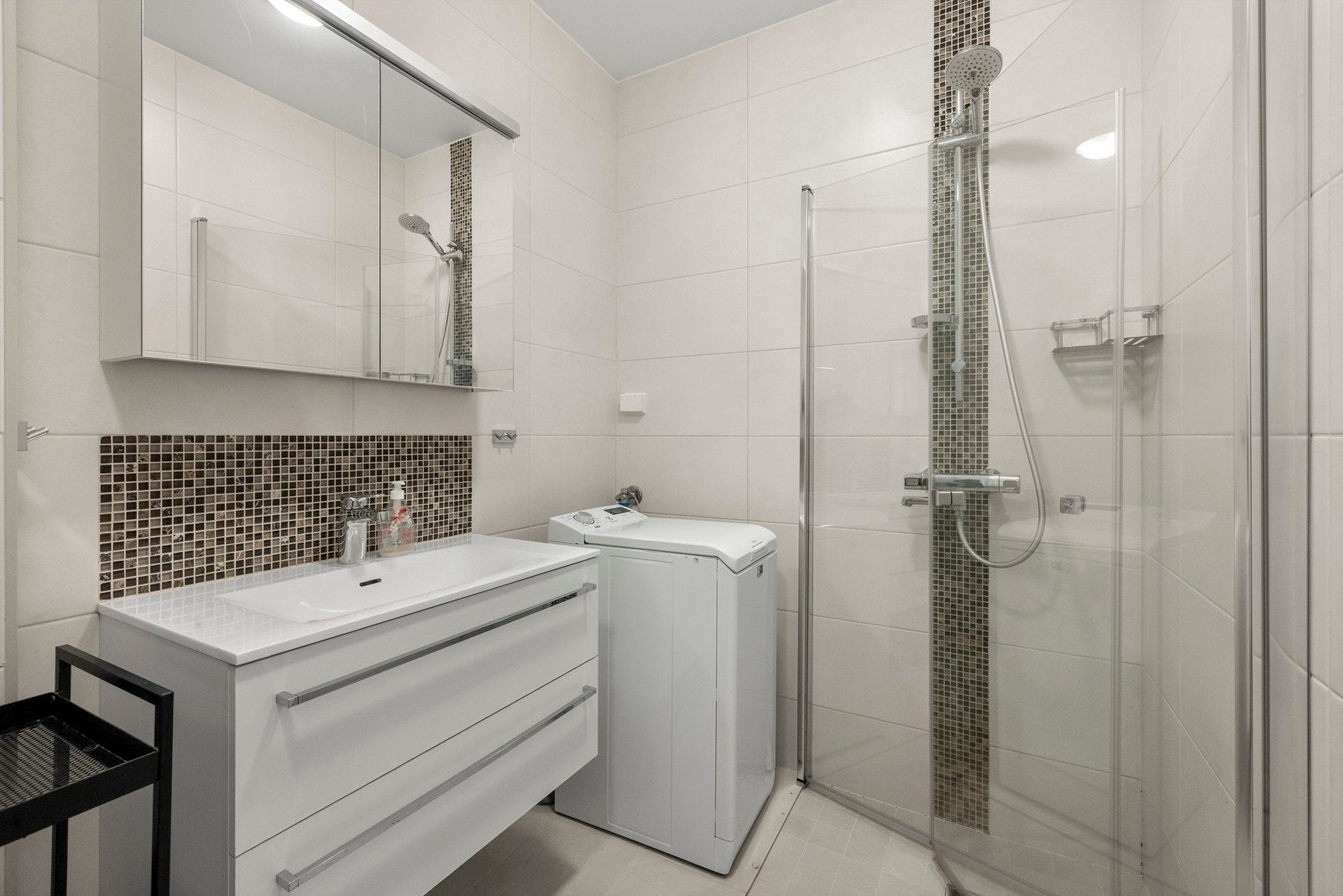 Badet er utstyrt med veggmontert toalett, opplegg for vaskemaskin og en nedsenket dusjsone med praktiske, svingbare glassdører. Galleribilde