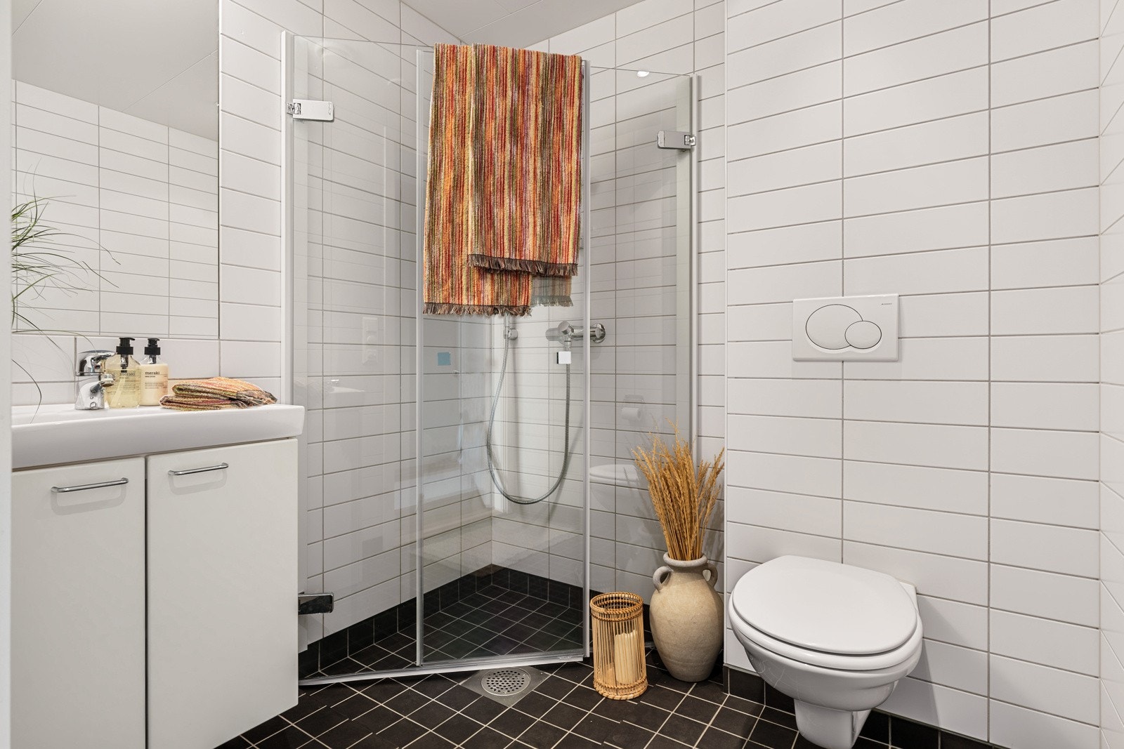 Badet er flislagt og er innredet med servant med underskap, vegghengt toalett og dusjhjørne med foldbare glassdører. Nye glassdører ble satt inn i 2025. Galleribilde