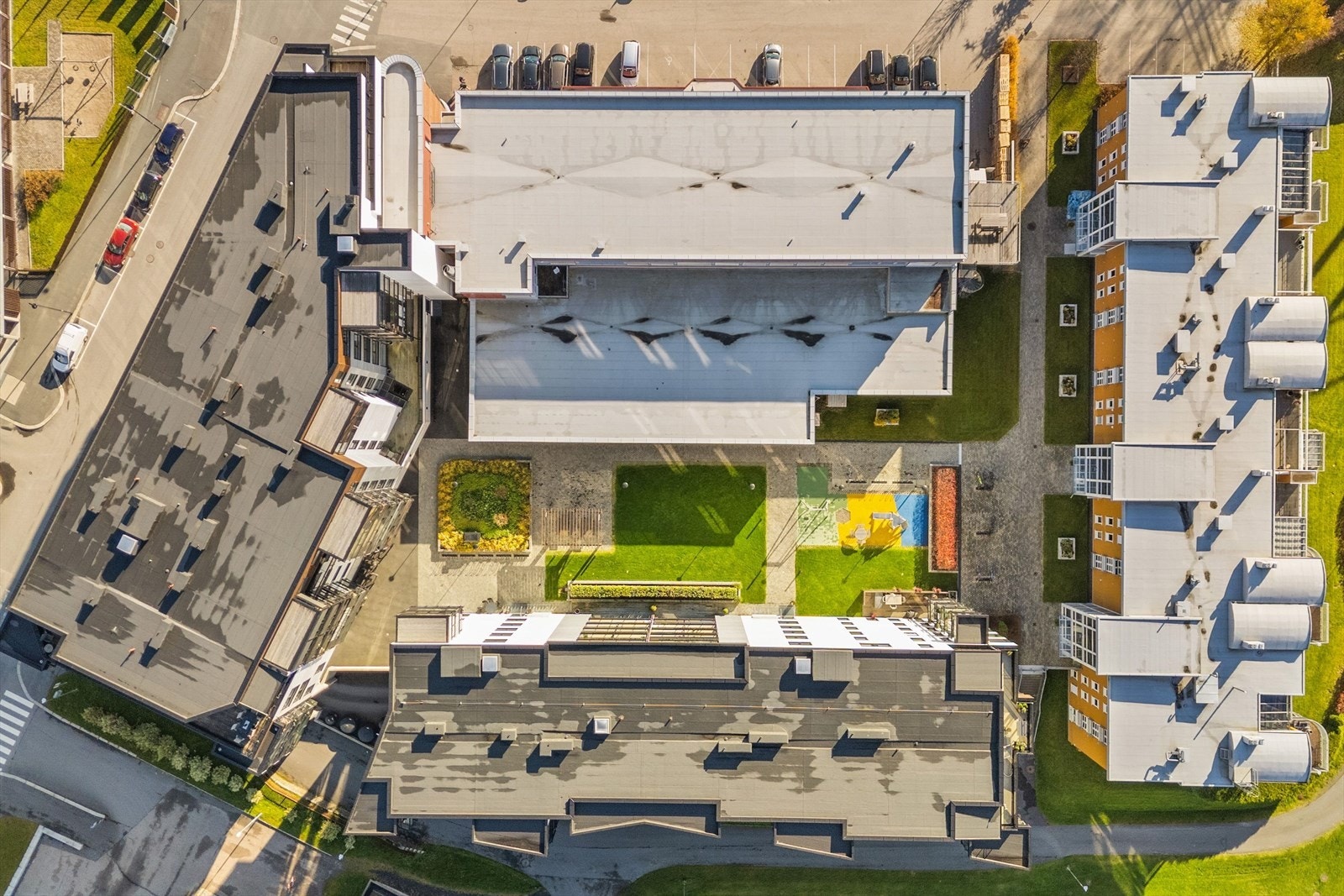 Leilighetsbygget sett fra luften. Her ser man det fine og pent opparbeidede fellesområdet, som har både sittebenker og lekeområder. Galleribilde