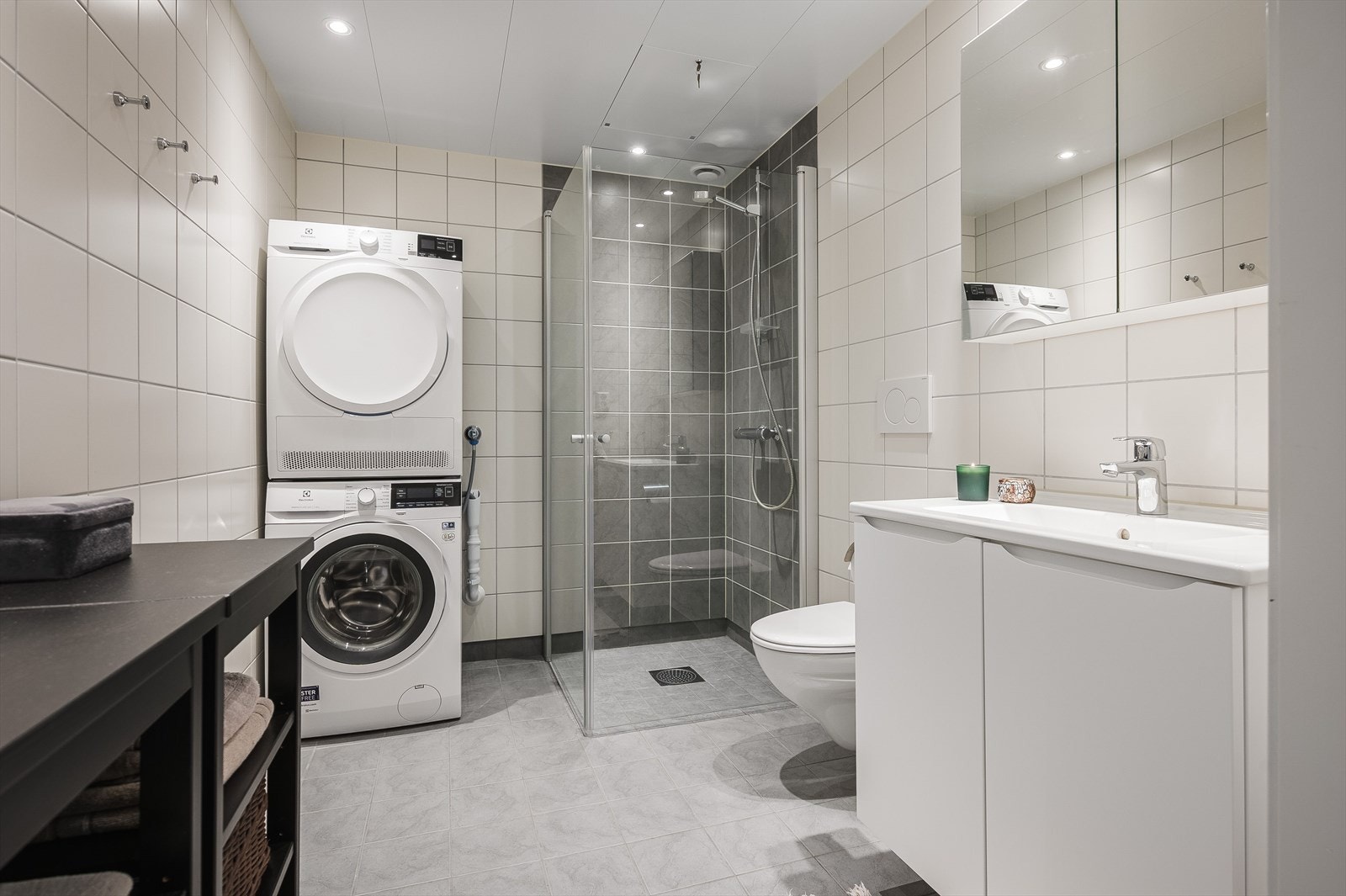 Flislagt bad/vaskerom med vegghengt toalett, dusj med innfellbare glassdører og servant i innredning med speilskap. Galleribilde