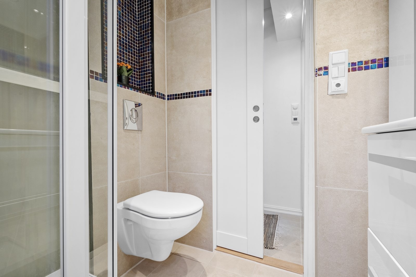 Badet er utstyrt med vegghengt toalett, helstøpt servant, skuffer under servant og dusjkabinett Galleribilde