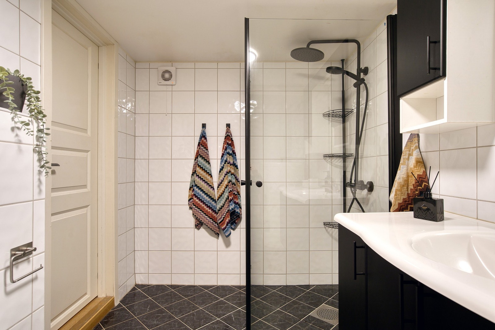 Flislagt bad/vaskerom med servantinnredning, dusjhjørne, vegghengt toalett, opplegg for vaskemaskin, utslagsvask og varmtvannsbereder. Galleribilde