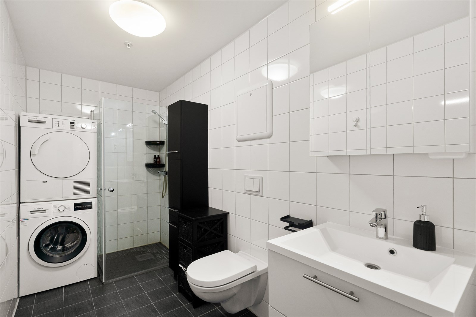 Badet er helfliset på vegger og gulv. Videre har badet vannbåren gulvvarme, avtrekk via det balanserte ventilasjonssystemet, vegghengt toalett og dusjhjørne med innfellbare glassdører. Baderomsinnredningene med speil og møblementet har skuffer. Galleribilde