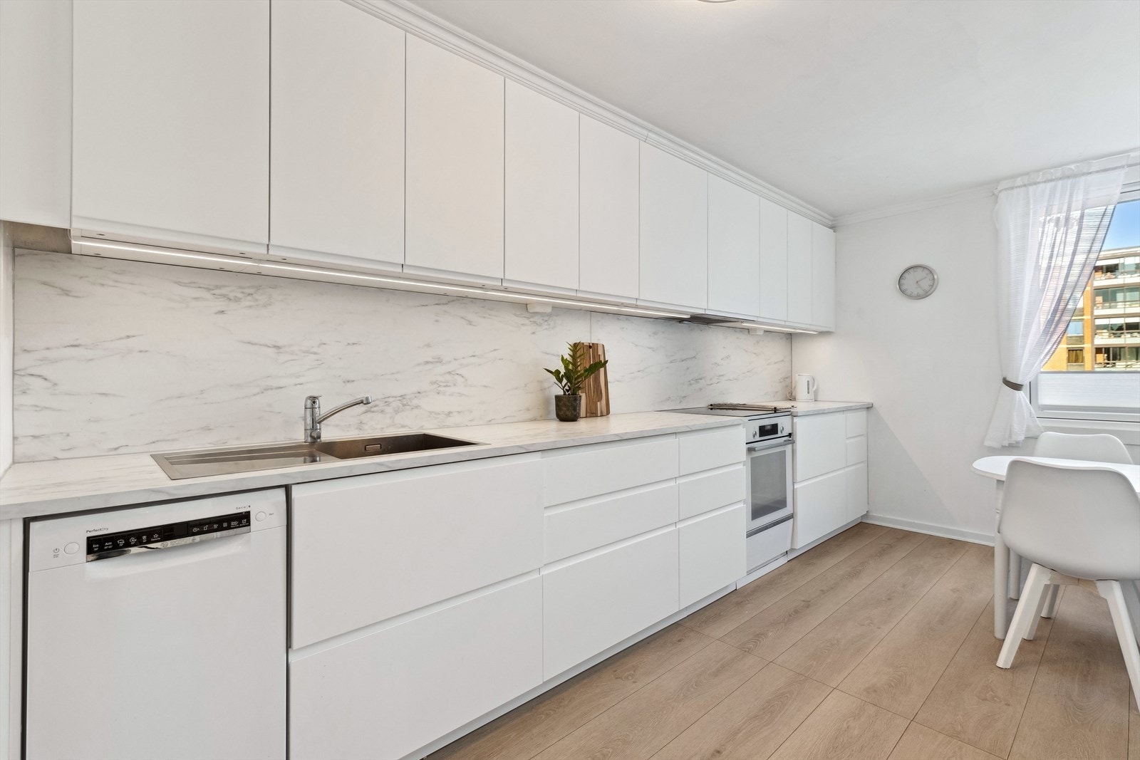 Kjøkken fra 2023 med takhøy kjøkkeninnredning, folierte fronter, laminat benkeplate, laminatplater over benken, kullfilterventilator og stål benkebeslag. Galleribilde