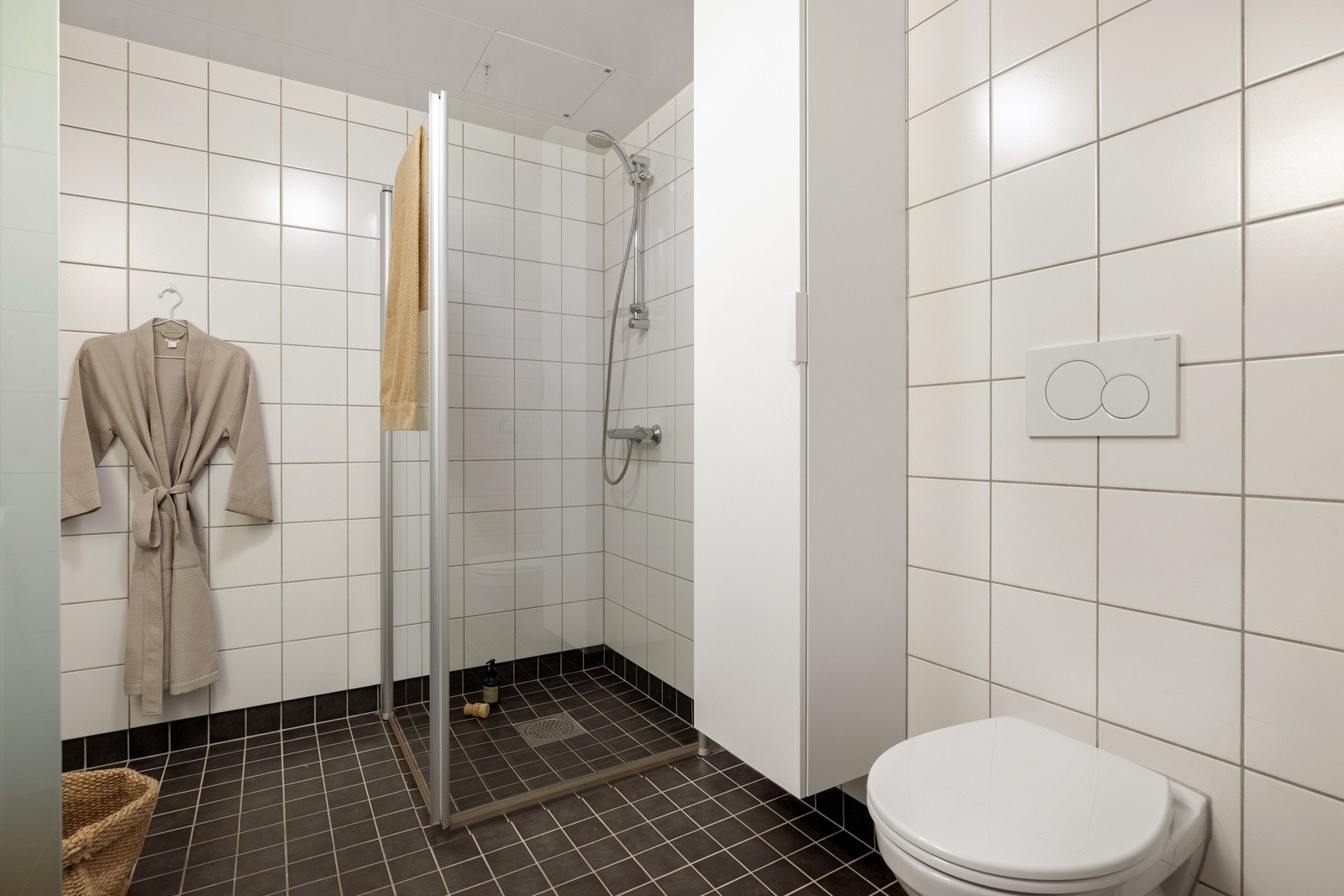 Badet er helfliset med vannbåren gulvvarme. Badet er innredet med vegghengt toalett, dusj med hengslede glassdører, opplegg for vaskemaskin og baderomsinnredning med heldekkende servant. Galleribilde