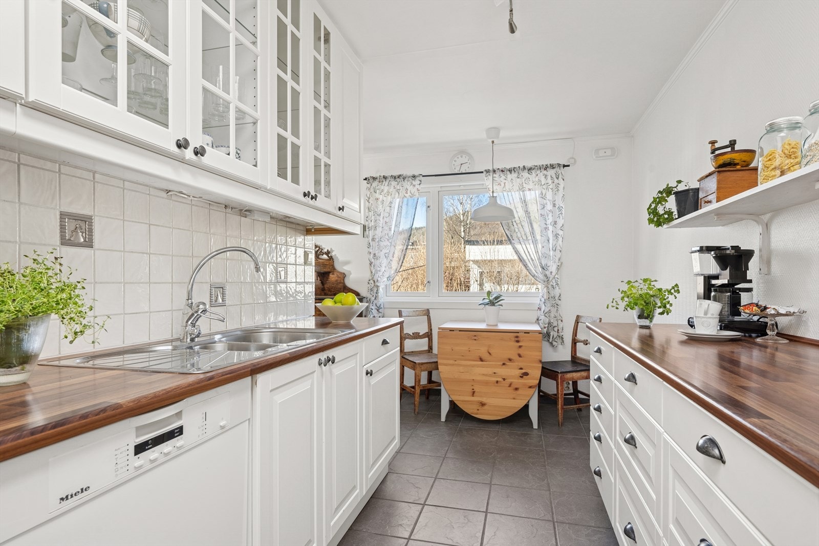 Kjøkkeninnredning med glatte fronter. Enkelte glassfronter i overskap. Fliser på vegg over benkeskap. Galleribilde