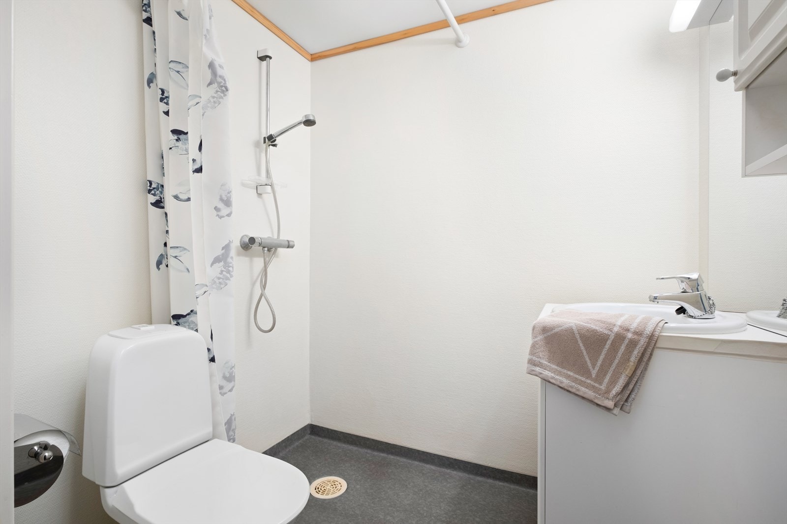 Badet er innredet med toalett, innredning med servant, åpen dusjsone med dusjgarnityr på vegg og dusjforheng Galleribilde