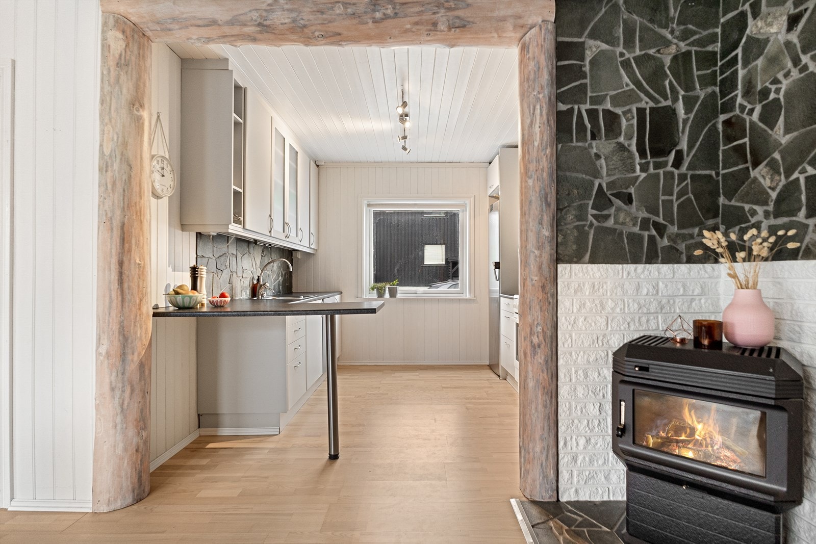 Kjøkkenet har en enkel øy med mulighet for sitteplasser. Legg merke til detaljen, der det er lagt dekor i form av tømmer som omramming i overgang mellom kjøkkenet og stuen. Galleribilde