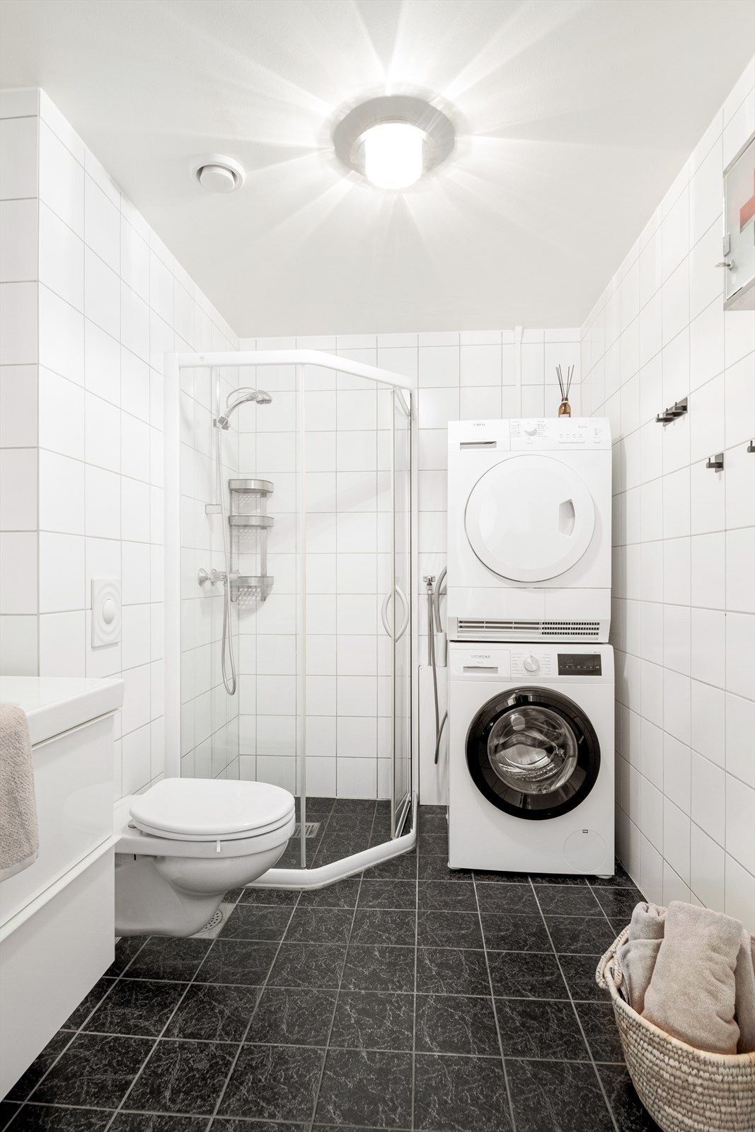 Badet er innredet med hvit servant med speil, vegghengt wc, dusjnisje med glassdører, samt opplegg for vaskemaskin og tørketrommel. Galleribilde