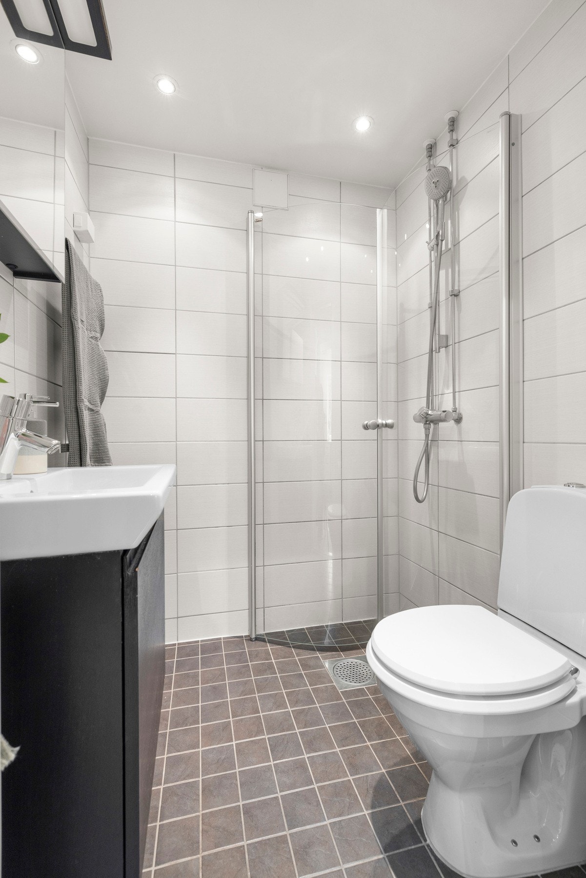 Flislagt baderom med servantinnredning, toalett og dusjhjørne med innfellbare glassdører Galleribilde