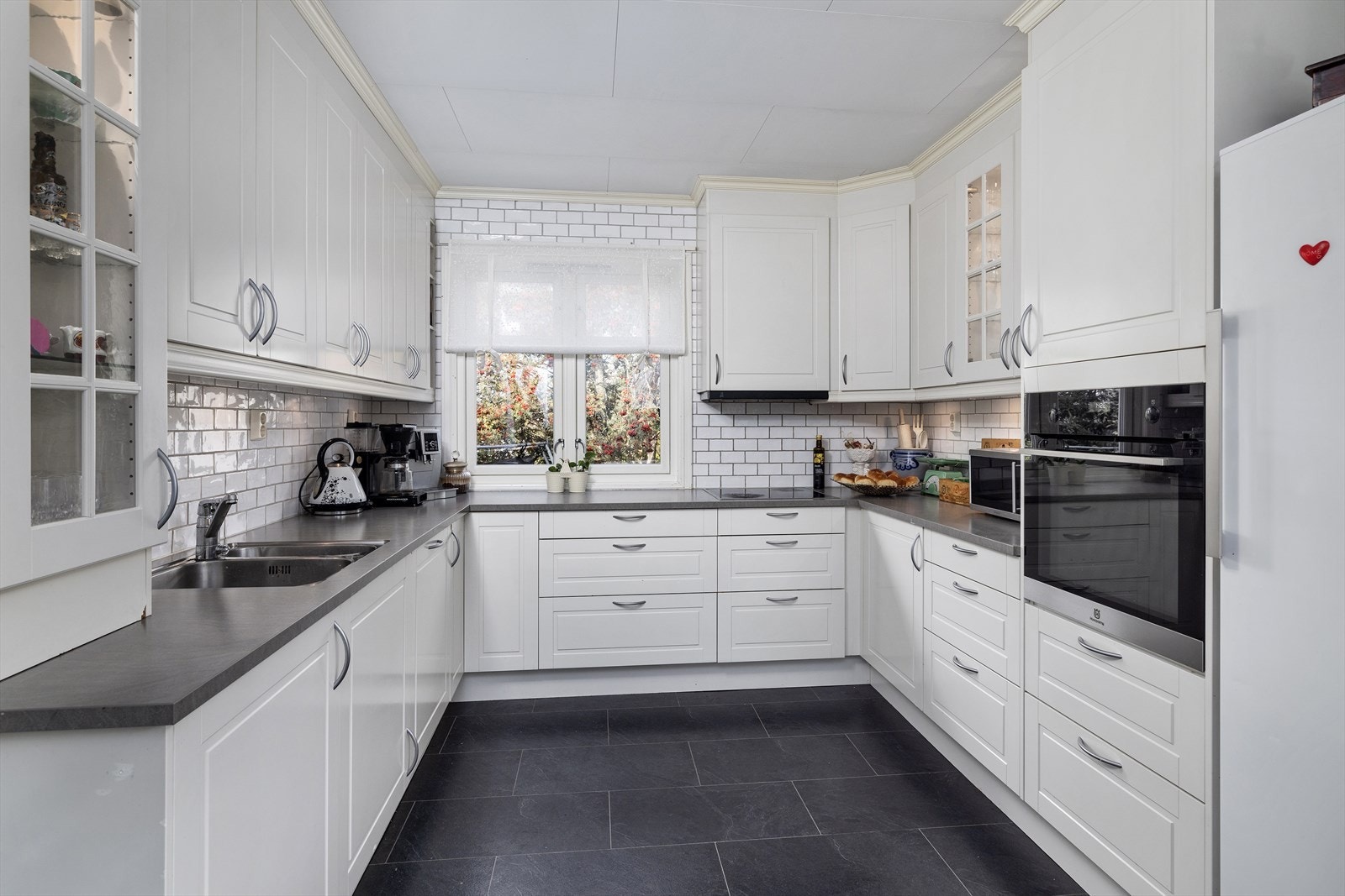 Det er lyse, profilerte fronter og en laminat benkeplate. Kjøkkenet er utstyrt med integrerte hvitevarer, inkludert oppvaskmaskin, platetopp, stekeovn, samt en kjøkkenventilator med avtrekk ut. Galleribilde