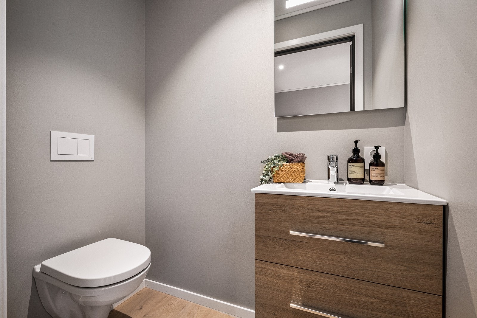 - Med adkomst fra gangen finner du et lite gjestetoalett med vegghengt toalett, servant med skuffer og speil med integrert belysning - Galleribilde