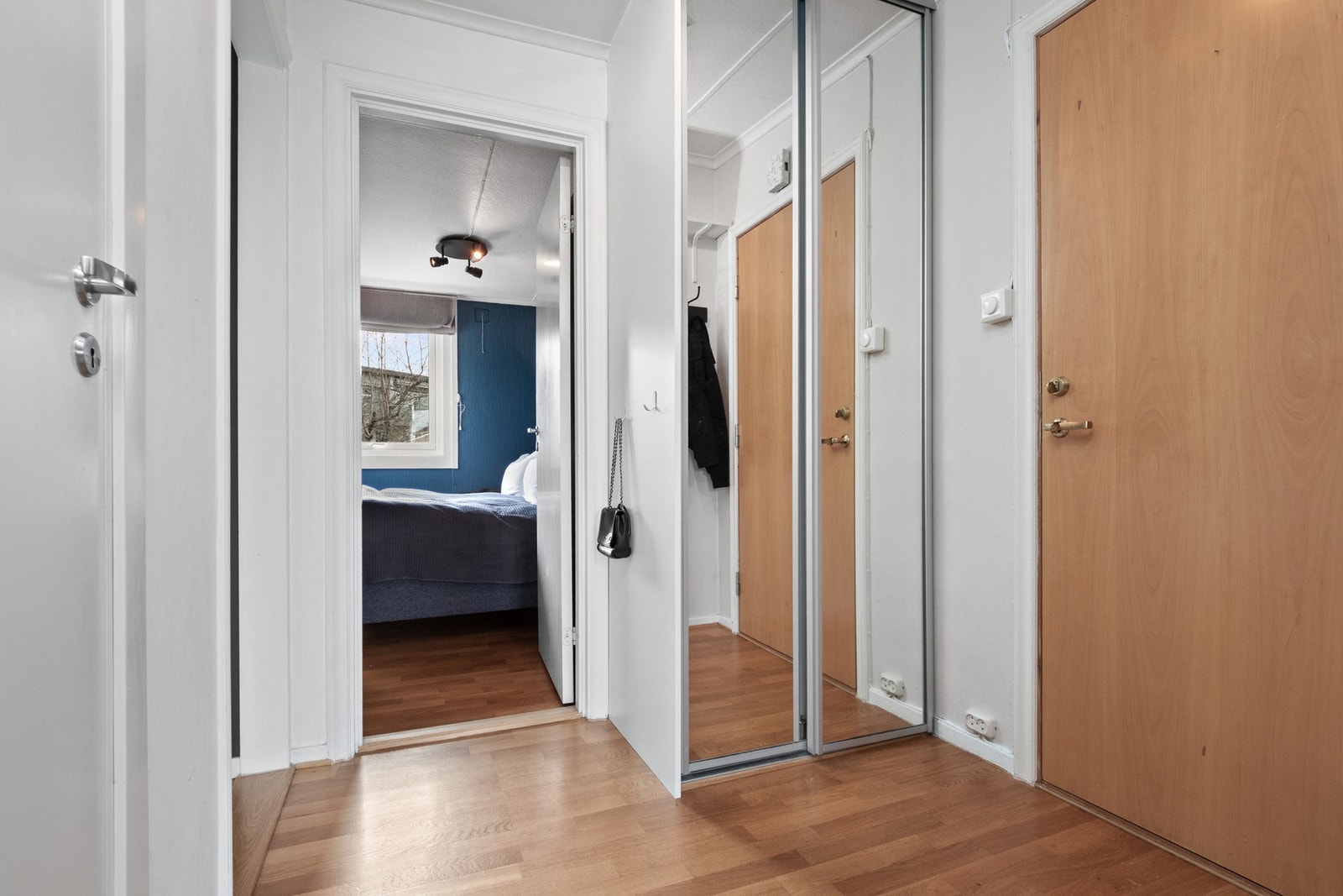 Entreen har parkettgulv, hvitmalte vegger og hvitmalt himling. I den ene veggen er det montert en skyvedørsgarderobe med speilfronter og på motsatt side er det knagger til yttertøy. Galleribilde