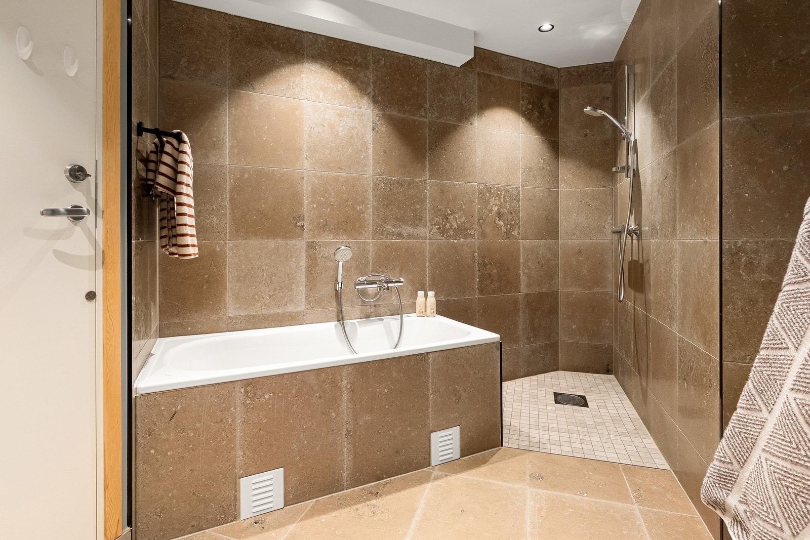 Store, beige fliser fra Lenngren Naturstein(Jura Grey Apollo) gir rommet et sofistikert uttrykk, mens innredningen er nøye utformet for å kombinere funksjonalitet med stilfullt design. Galleribilde