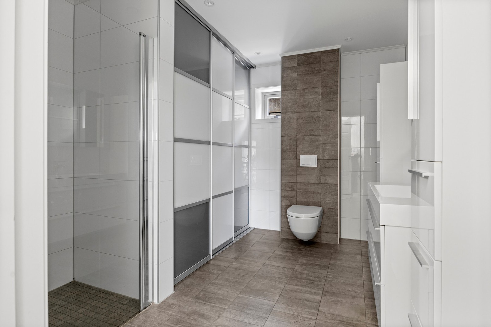 Bad/vaskerom - 9 kvm. Flislagte overflater med varme i gulv. Downlights. Vaskeromsløsning skjult bak skyvedør. Galleribilde