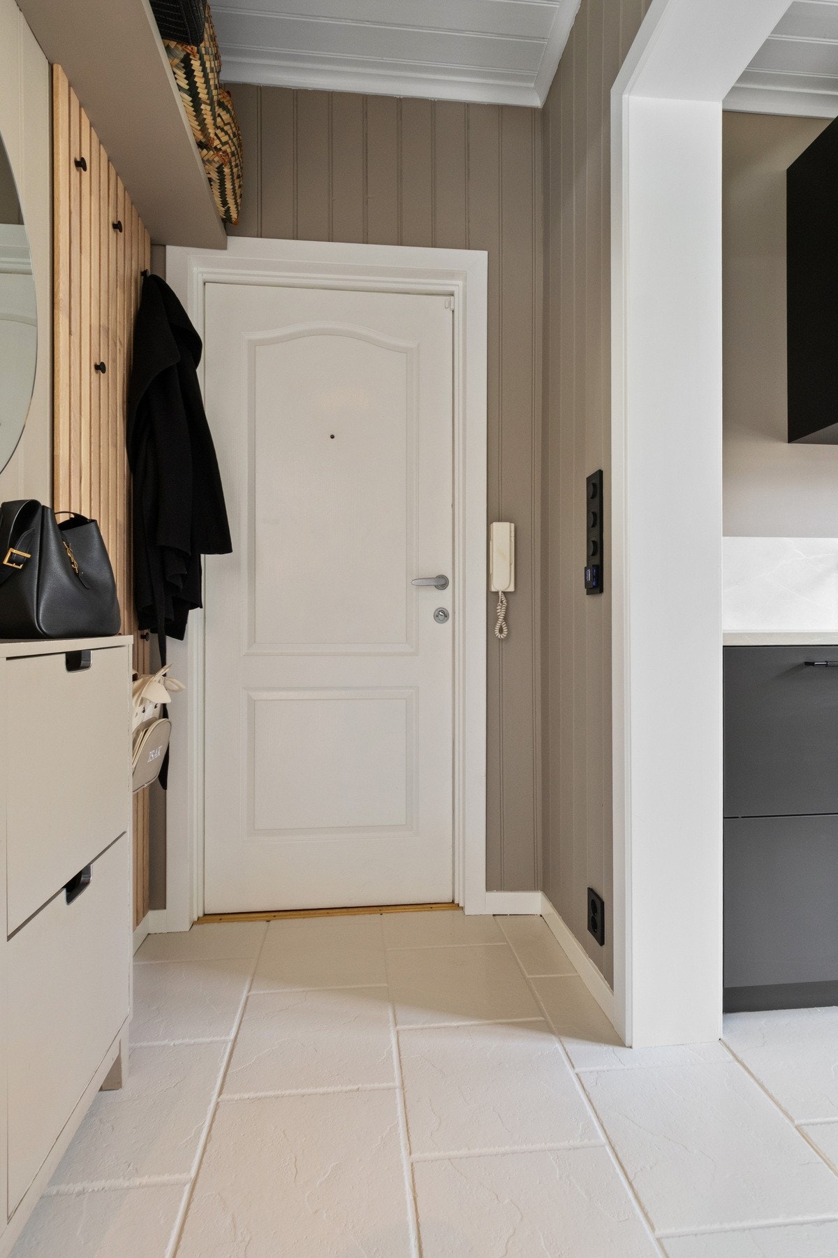 Vel inne gir gangen et godt førsteinntrykk, med dempet brunbeige (greige) tone og varme under hvite gulvfliser. Galleribilde