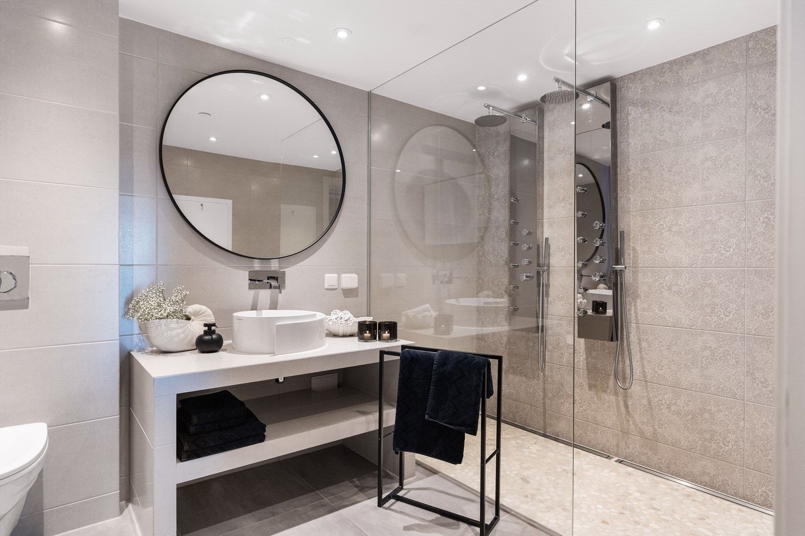 Rommet er utstyrt med lekker servantbenk med rund servantbolle, åpen dusjløsning med to regnfallsdusjer, veggmontert toalett samt opplegg for vaskemaskin og tørketrommel. Galleribilde