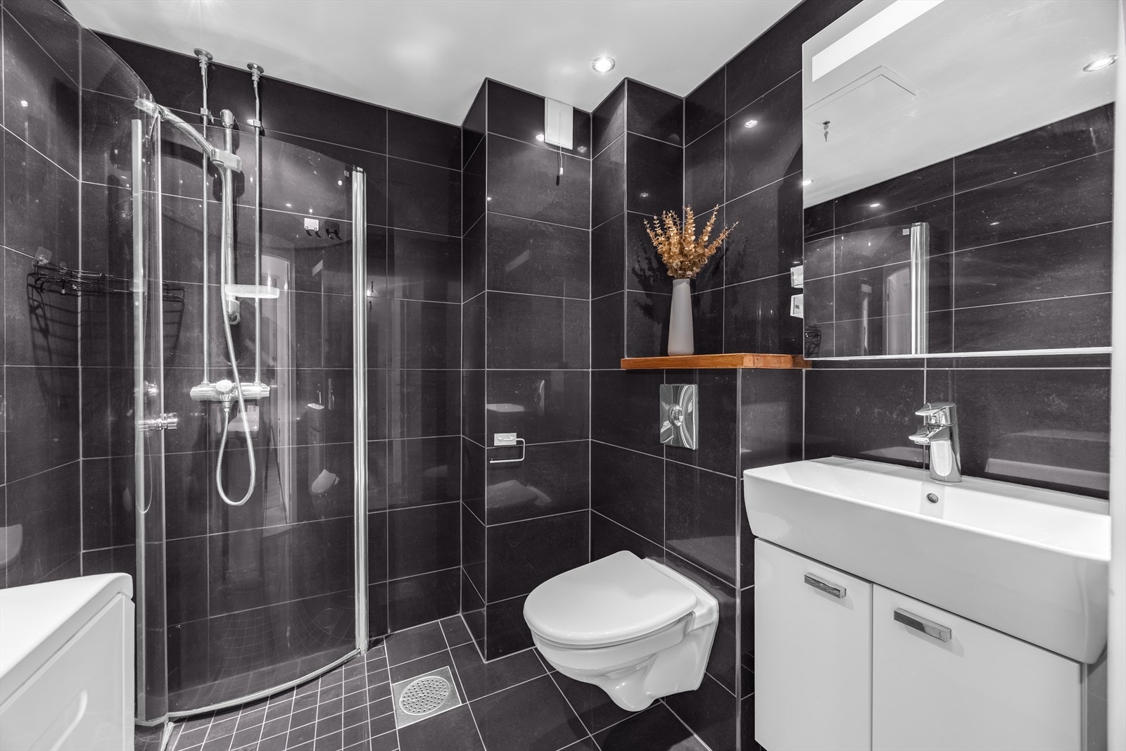 Innredningen består av vegghengt klosett, servant med underskap, speilskap og et praktisk dusjhjørne med svingbare glassdører. Galleribilde