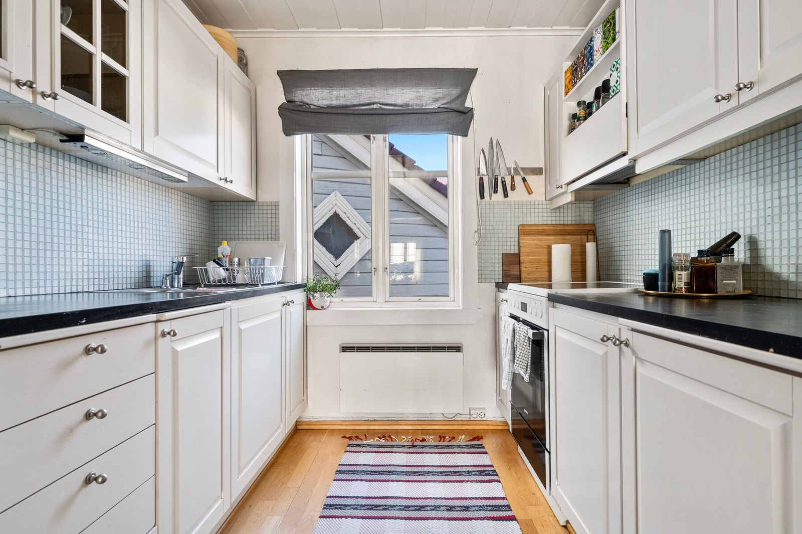 Kjøkkenet har hvite, profilerte heltrefronter, vitrineskap, en sortmalt heltre benkeplate og nedfelt oppvaskkum. Galleribilde