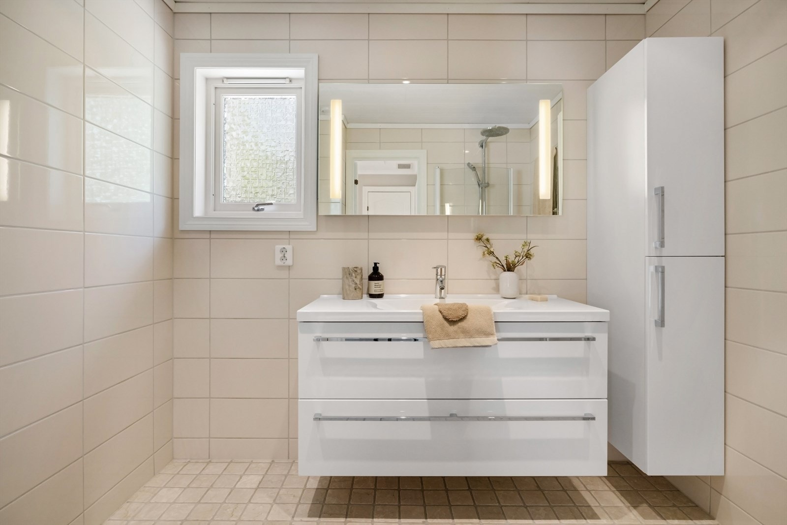Badet inneholder servant i møblement, veggskap, speil med belysning og dusjhjørne med dører i klart glass. Galleribilde