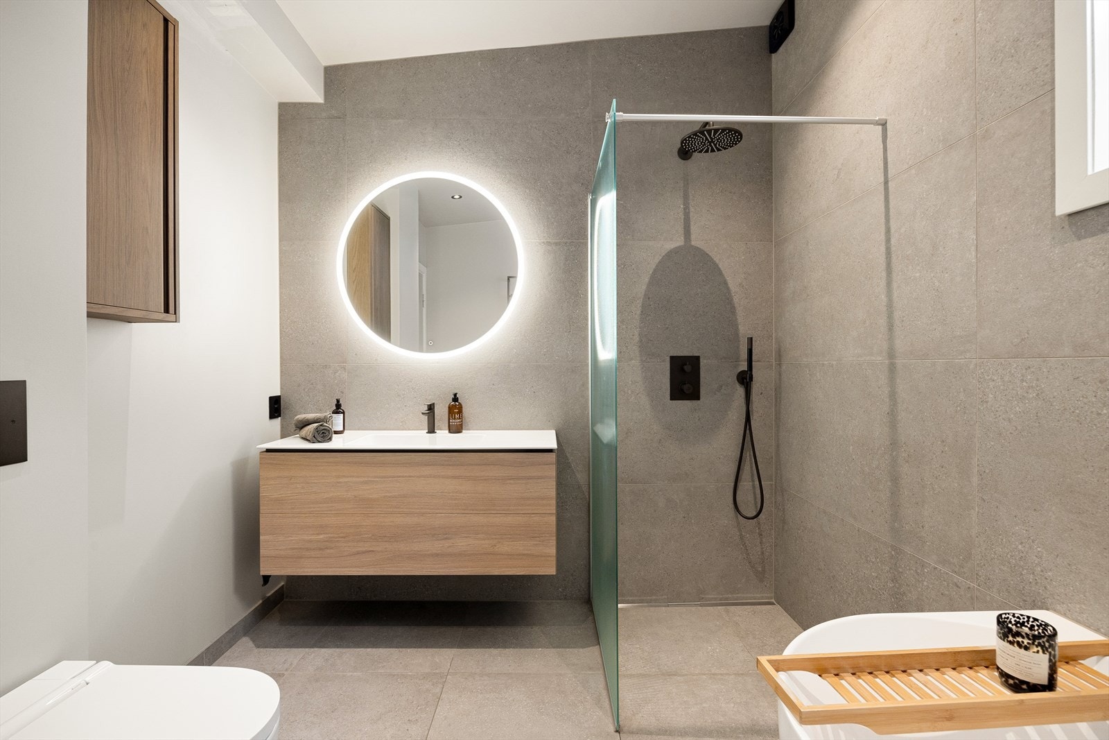 Badet er utstyrt med vegghengt toalett, dusj med både rainfall og håndholdt dusjhode, servant med underskap, ekstra veggskap og badekar. Galleribilde