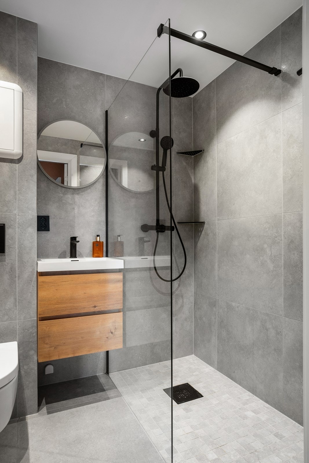 Rommet er innredet med dusjhjørne med glassvegg, vegghengt toalett og baderomsinnredning med nedsenket servant og speil Galleribilde