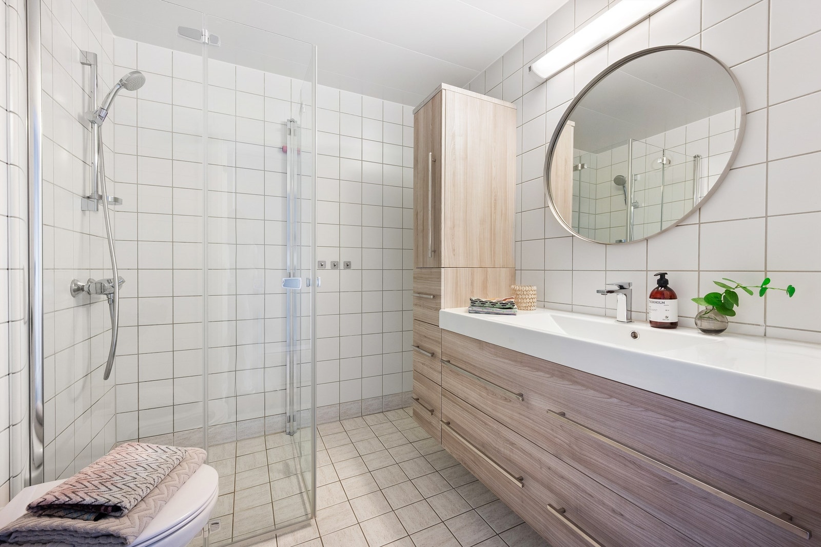 Over servanten er det speil med overlys og stikkontakt på vegg. Videre har badet dusjhjørne med innfellbare glassdører og vegghengt toalett. Galleribilde