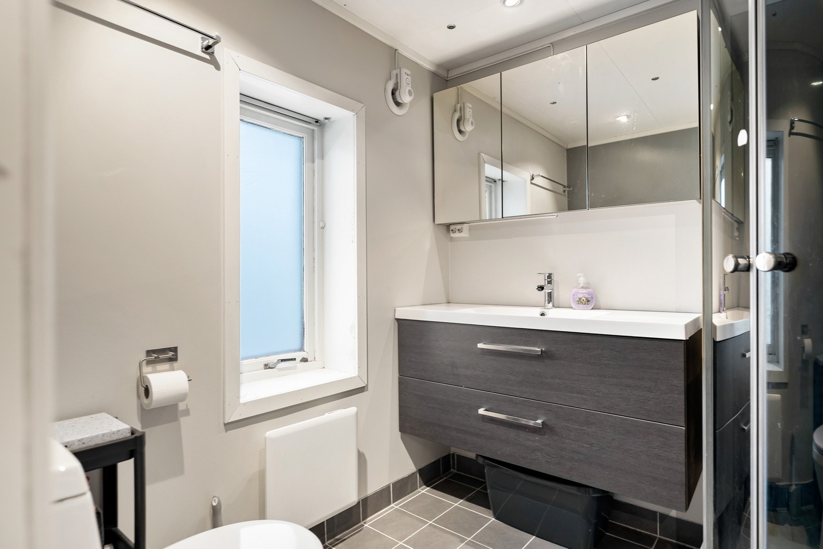 Baderom med vegghengt servantinnredning og dusjkabinett i hjørnet. Flislagt gulv med gulvvarme Galleribilde