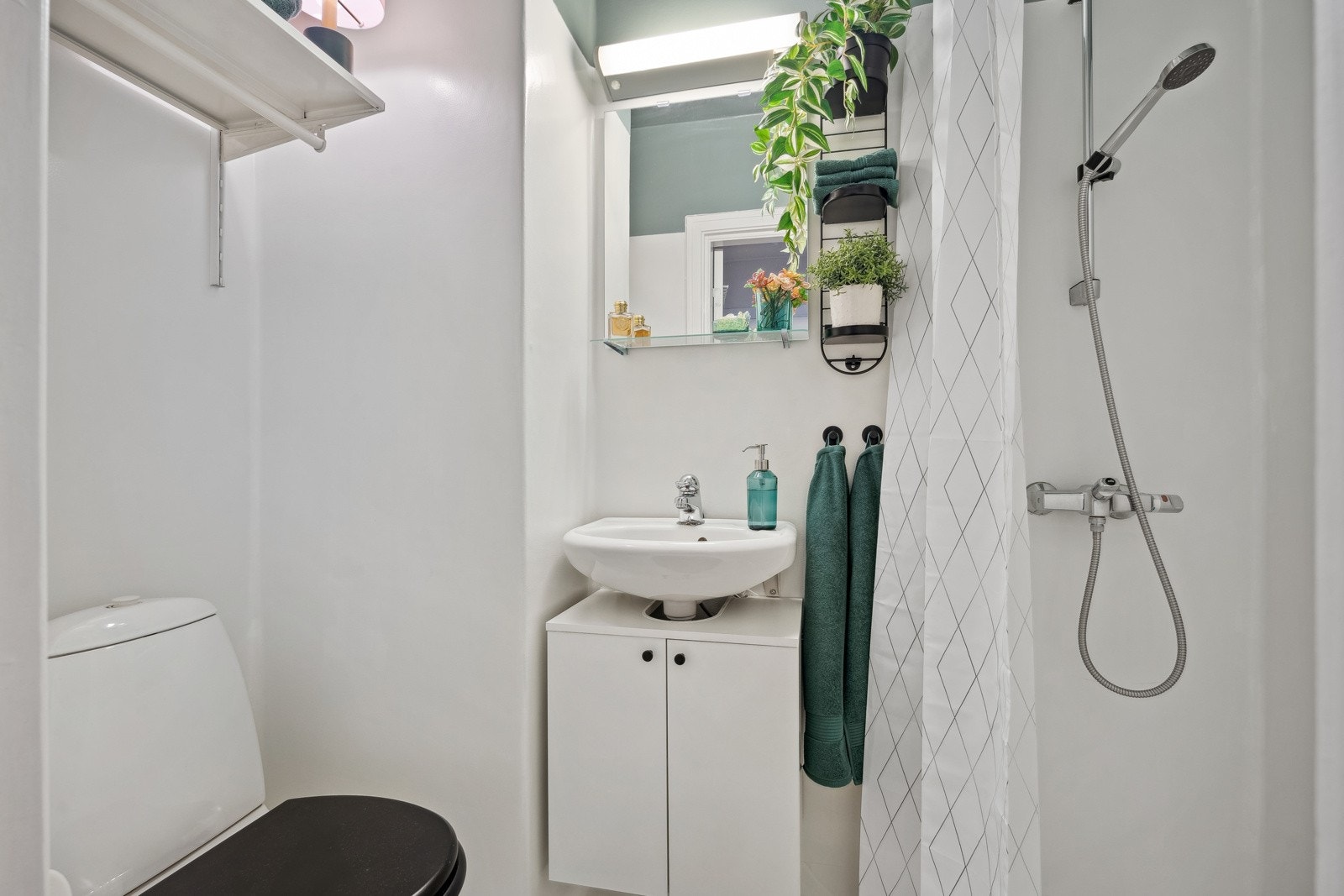 Lyst baderom utstyrt med vegghengt servantinnredning, speil med overlys, dusjhjørne og toalett. Galleribilde