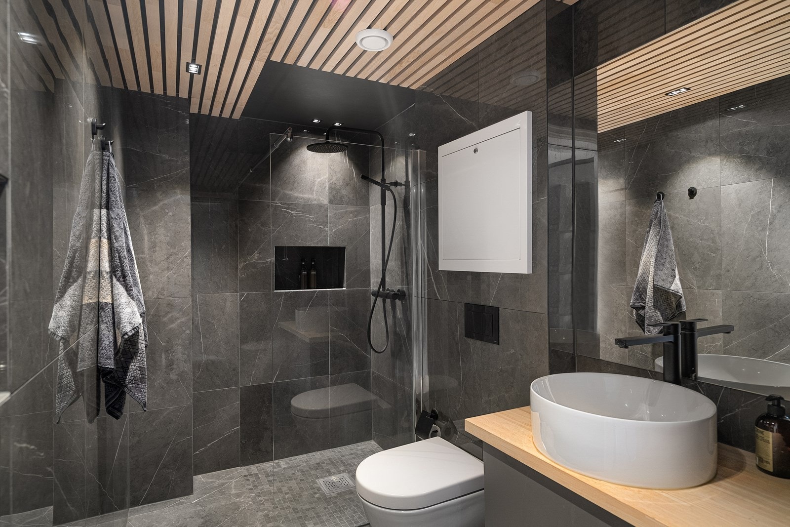 Badet er innredet med heltre benkeplate med rund servant, speil med belysning, veggmontert toalett og dusjsone Galleribilde
