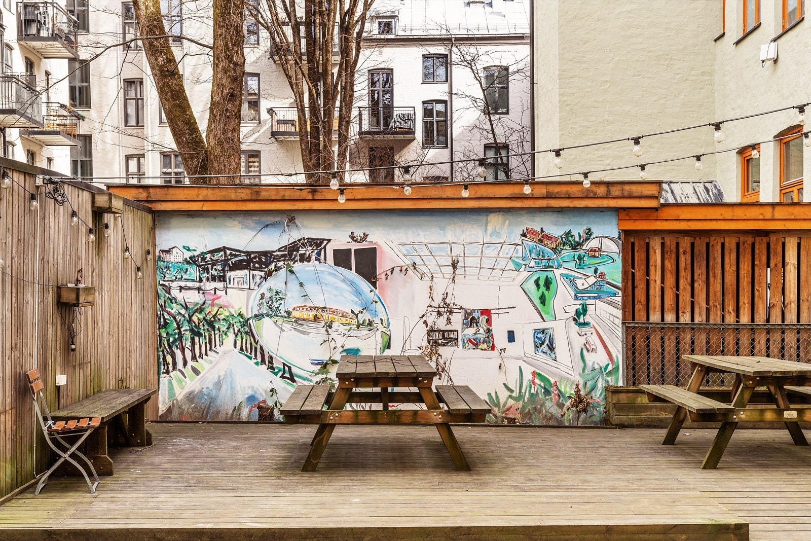Hyggelig bakgård med belegningsstein, hevet terrasse, skillevegger, belysning og flere sitteplasser med bord Galleribilde